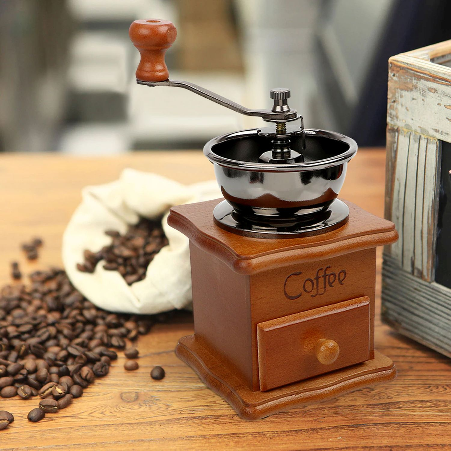 Kaffeemühle mit Holzsockel und Schublade. Kaffeebohnen um die Mühle verstreut.