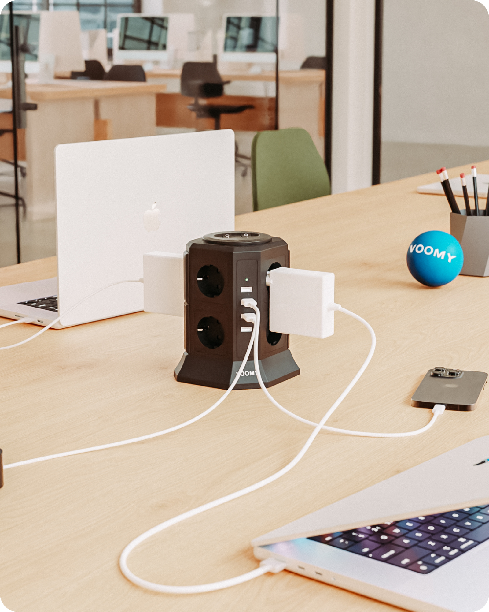 Schwarze Steckdosenleiste mit mehreren Steckdosen, USB-Anschlüssen und weißem Ladegerät auf einem Schreibtisch.