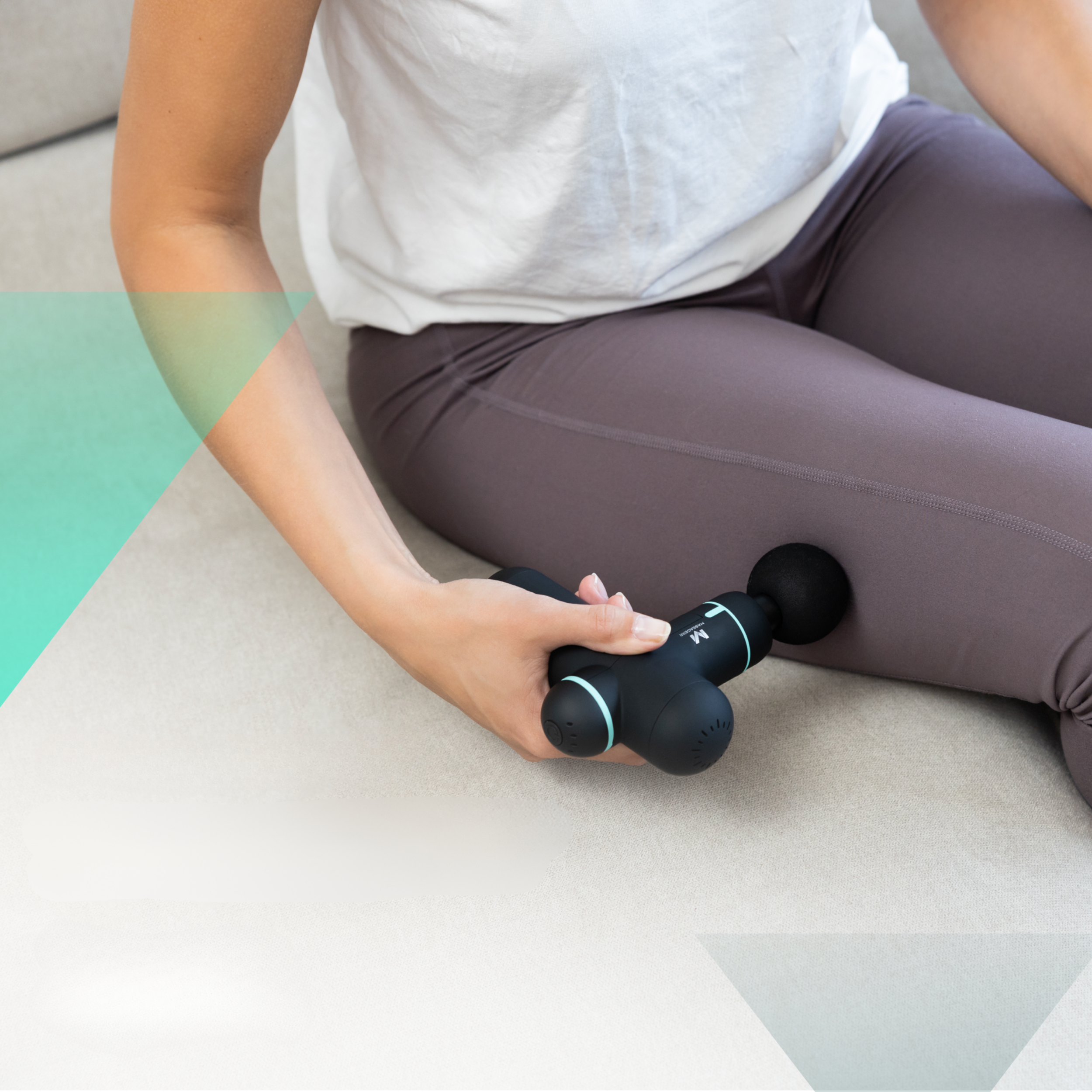 A person using a black massage gun on their leg, while seated on a sofa.