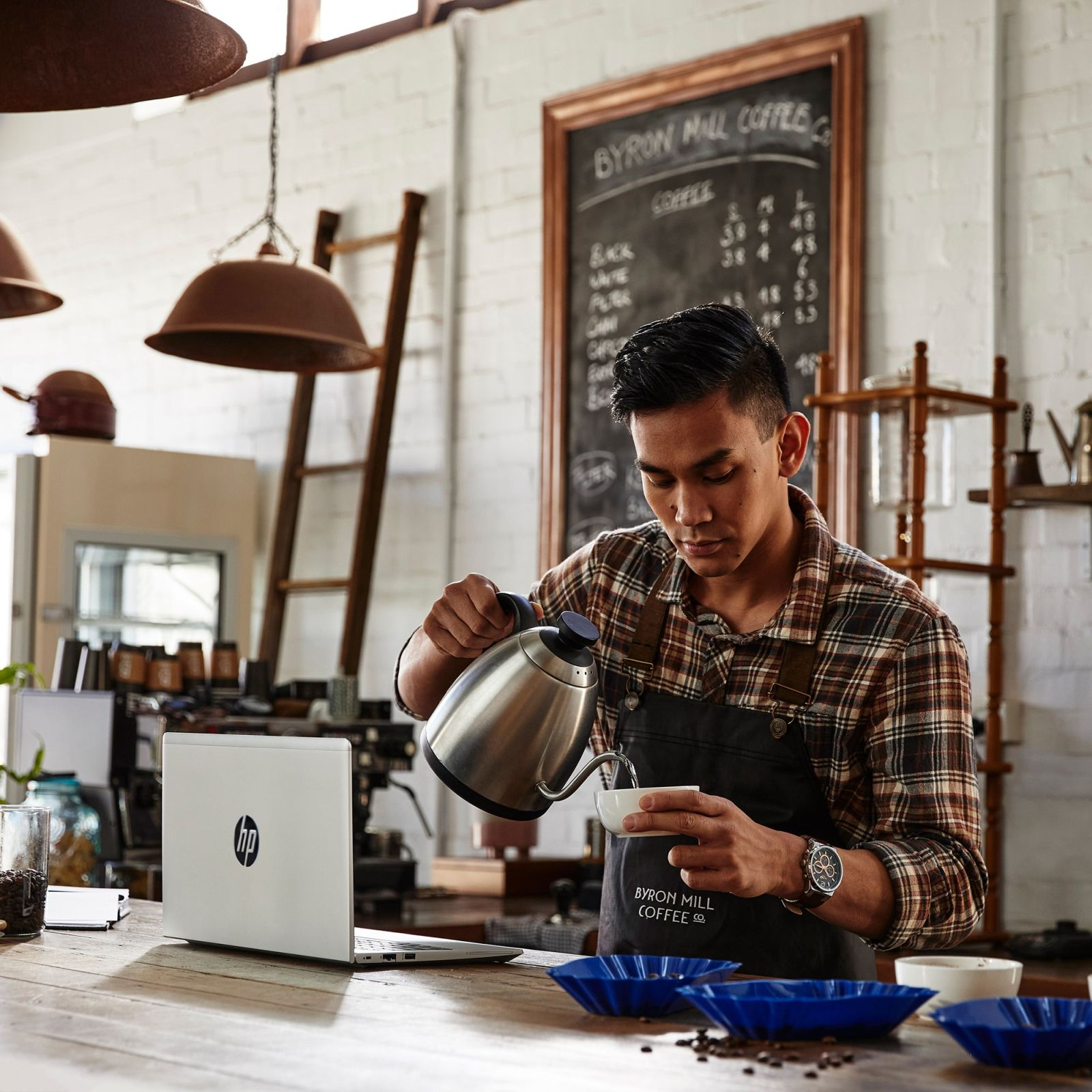 Un barista che versa caffè in una tazza con un laptop sul bancone.