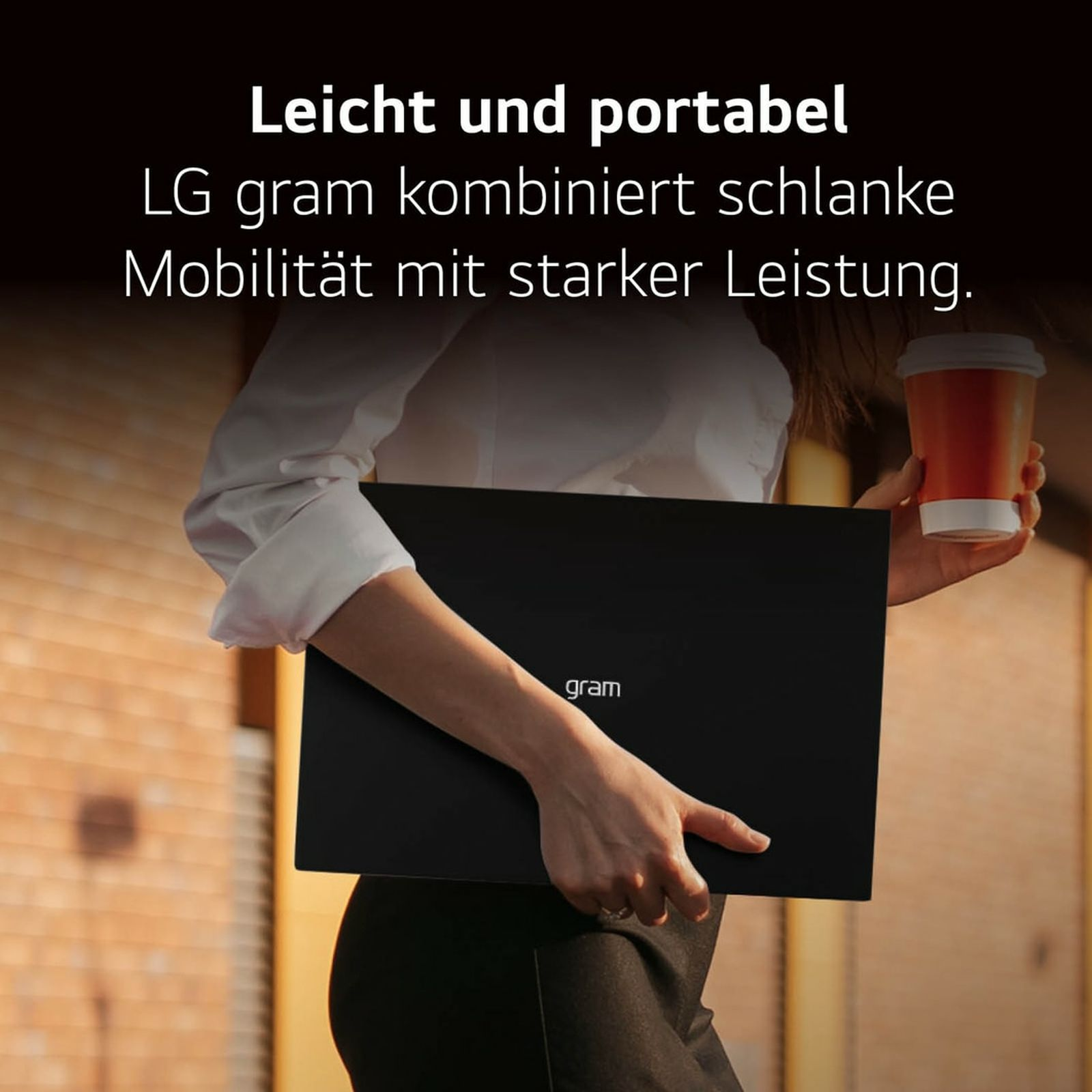 Eine Frau hält einen schwarzen Laptop und eine Kaffeetasse, steht vor einem Gebäude.
