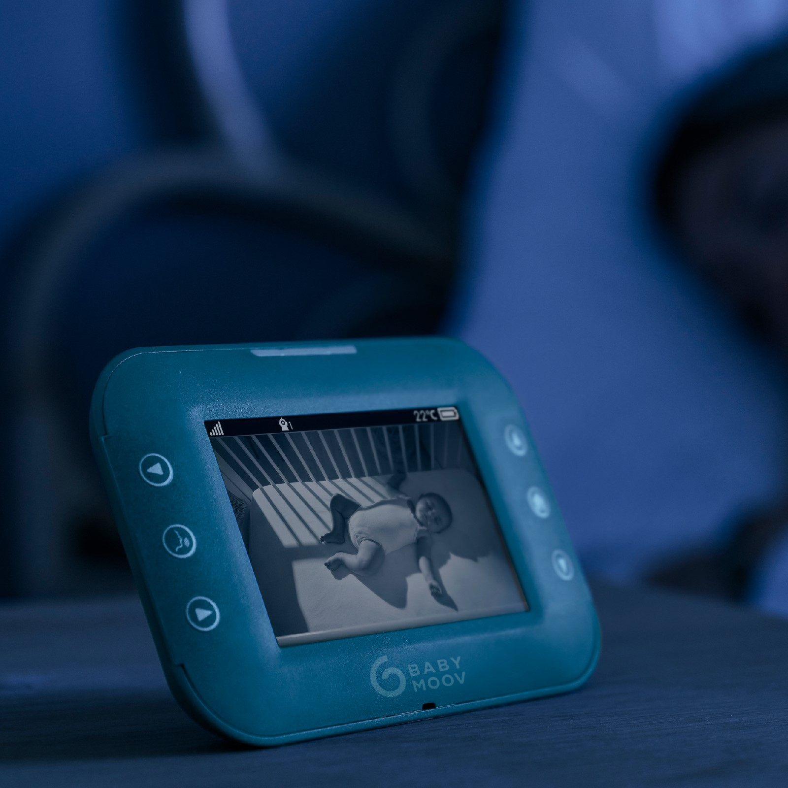 Ein Babyphone, das ein Baby in einem Kinderbett zeigt, mit einer Person im Hintergrund.
