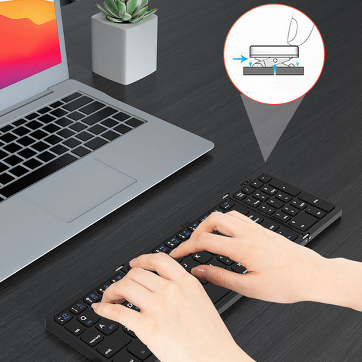 Hände tippen auf einer schwarzen, faltbaren Tastatur neben einem Laptop. Ein Diagramm in der Ecke.