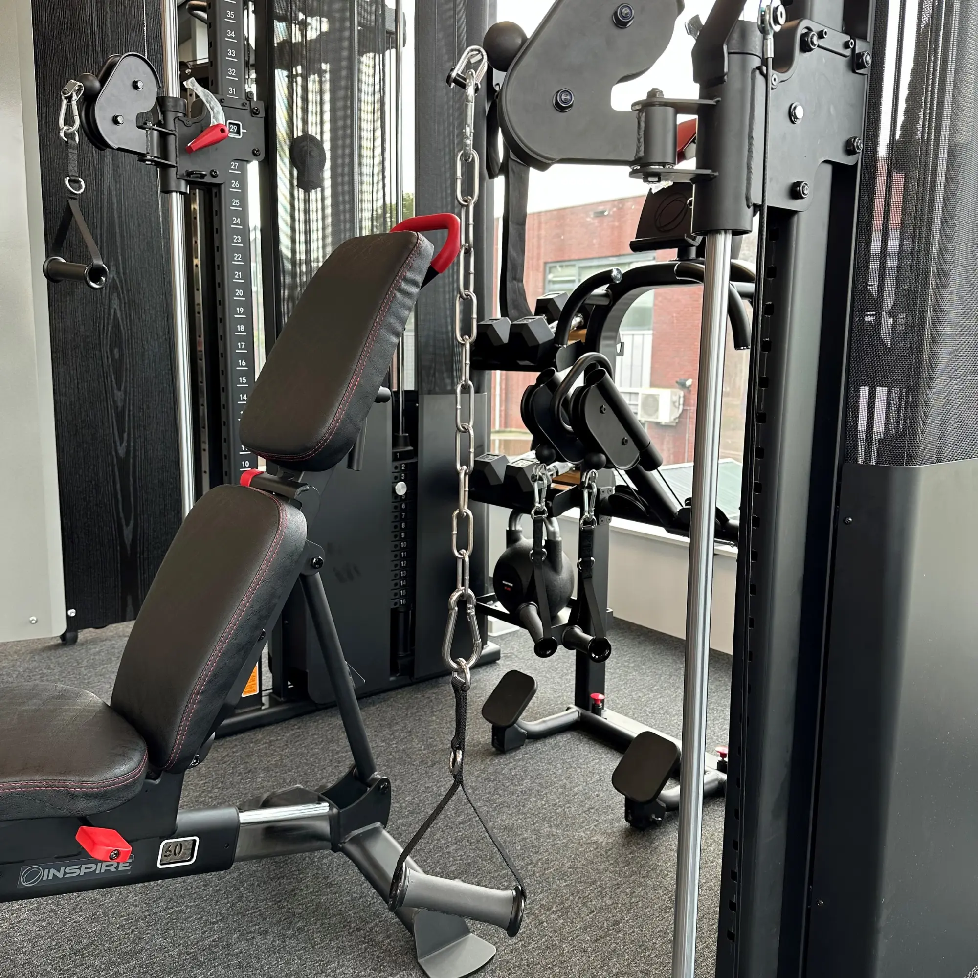 Gym interior. Gym equipment is visible: weight machine, benches, weights, and chains.