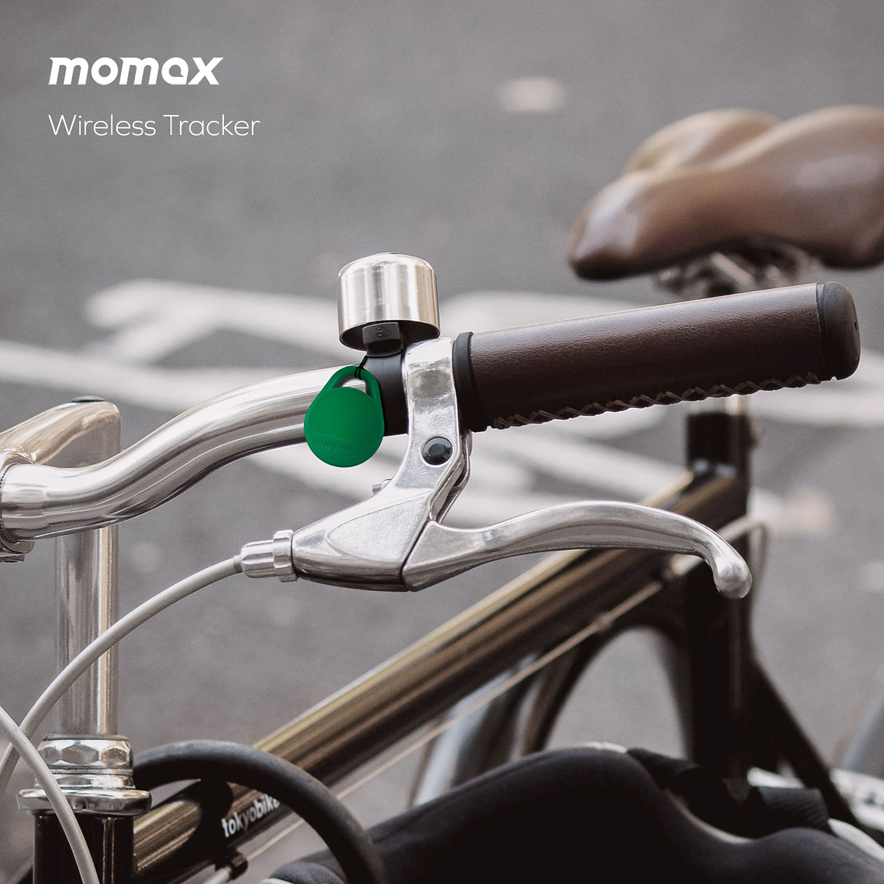 A bicycle handlebar with a bell, a green tag, and a brake lever. The background is blurred.