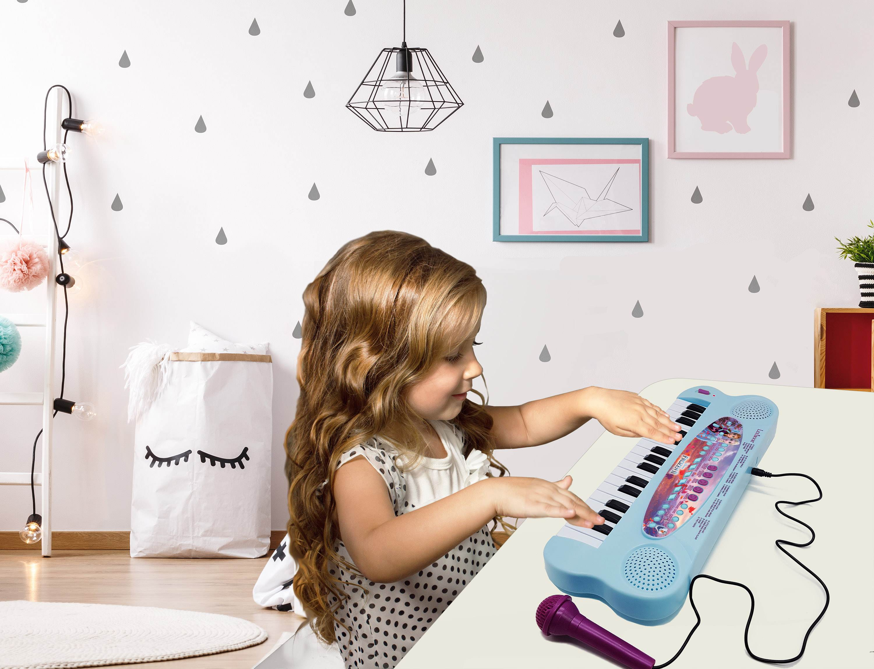 Una niña pequeña toca un piano de juguete. La habitación tiene una pared blanca con pegatinas de gotas.