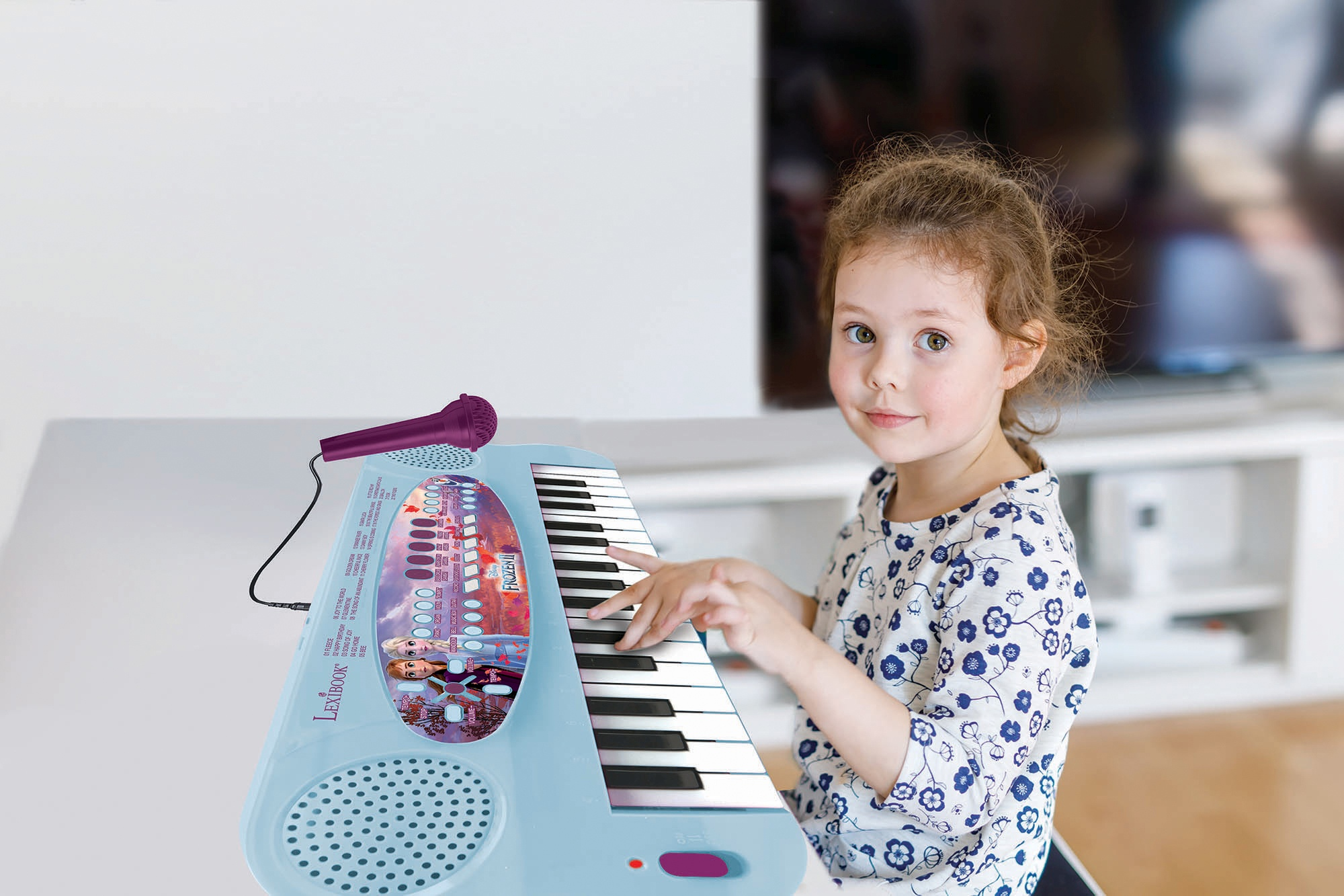 Una niña tocando un piano de juguete azul con un micrófono, sonriendo.