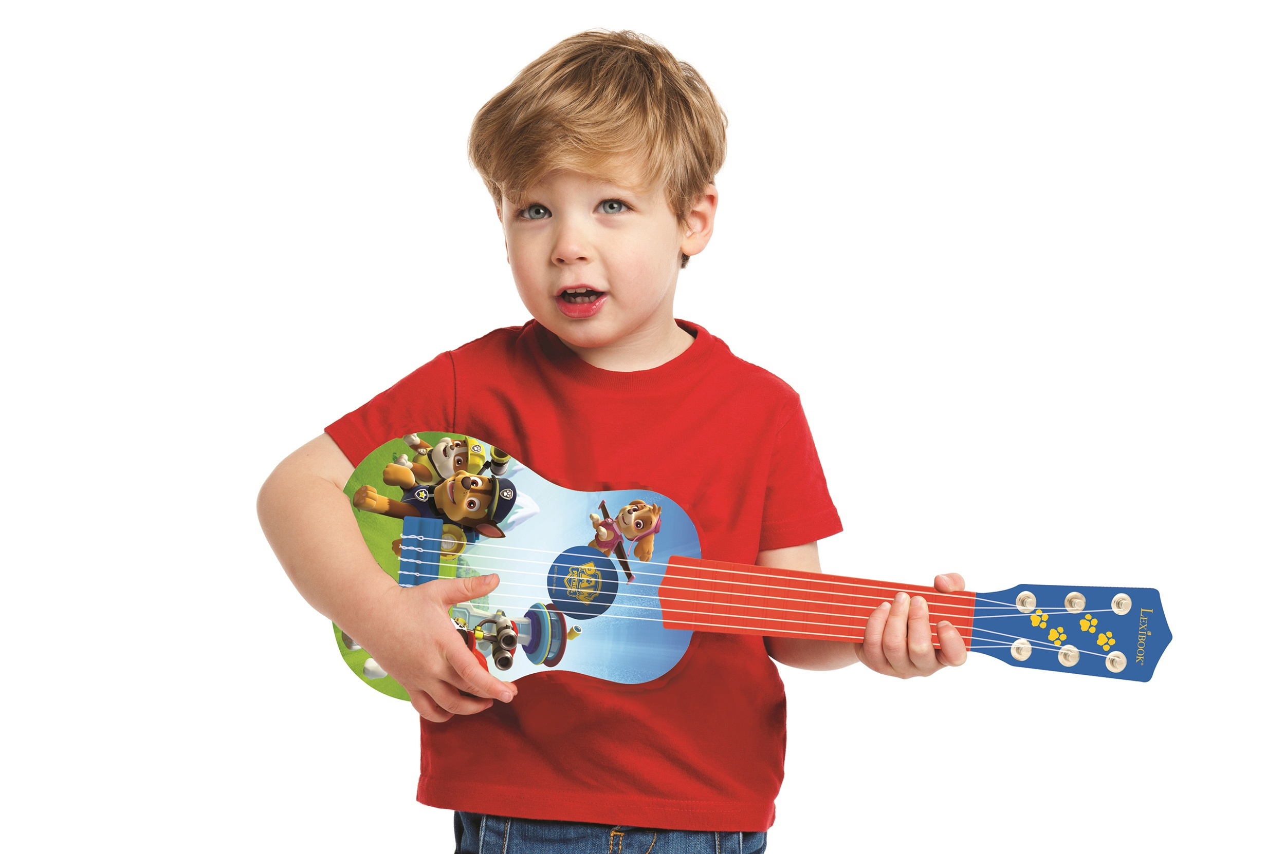 Mały chłopiec trzymający zabawkę gitarę z postaciami z Psiego Patrolu, patrzący w górę, czerwona koszulka.