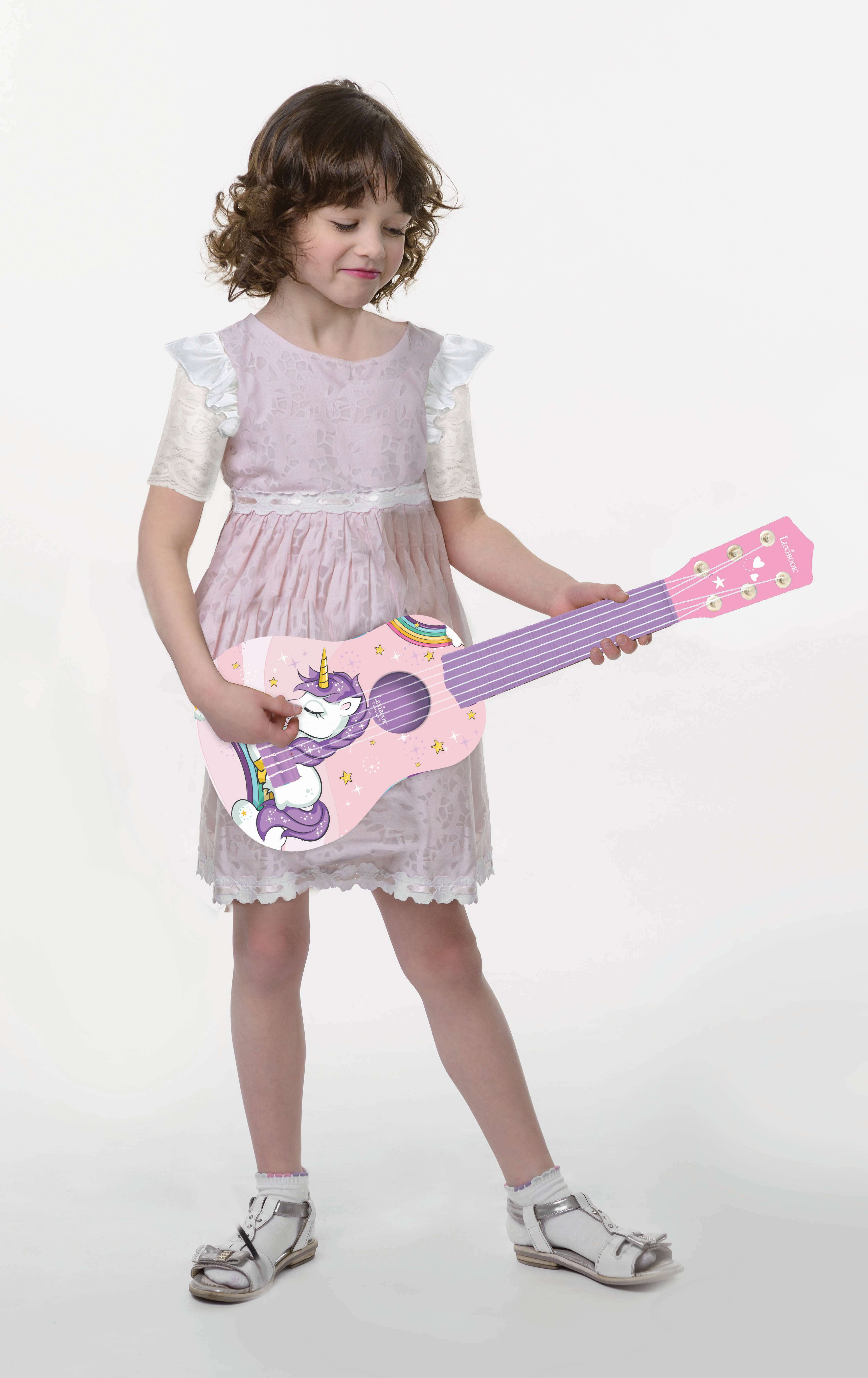 Una niña con un vestido rosa sostiene un ukelele rosa decorado con un unicornio y un arcoíris.
