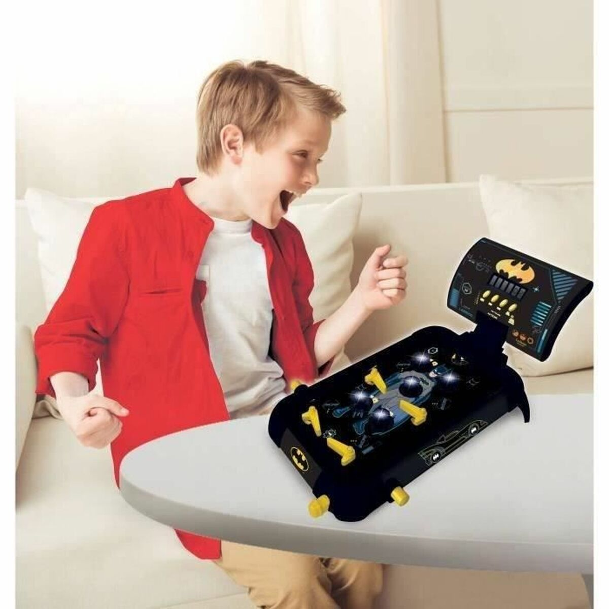 Ragazzo che gioca a un flipper di Batman. Il gioco è su un tavolo bianco. Il ragazzo è eccitato.