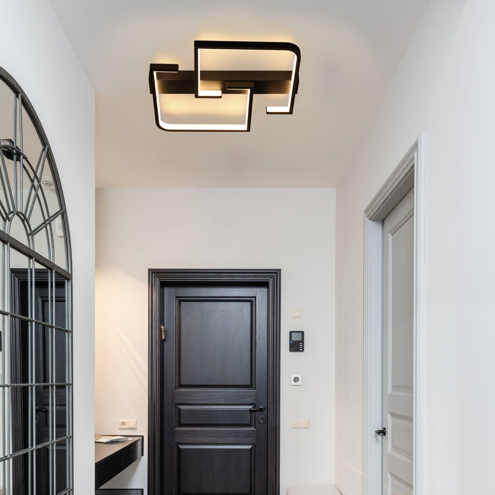 Pasillo con puerta negra, espejo y moderna lámpara de techo.