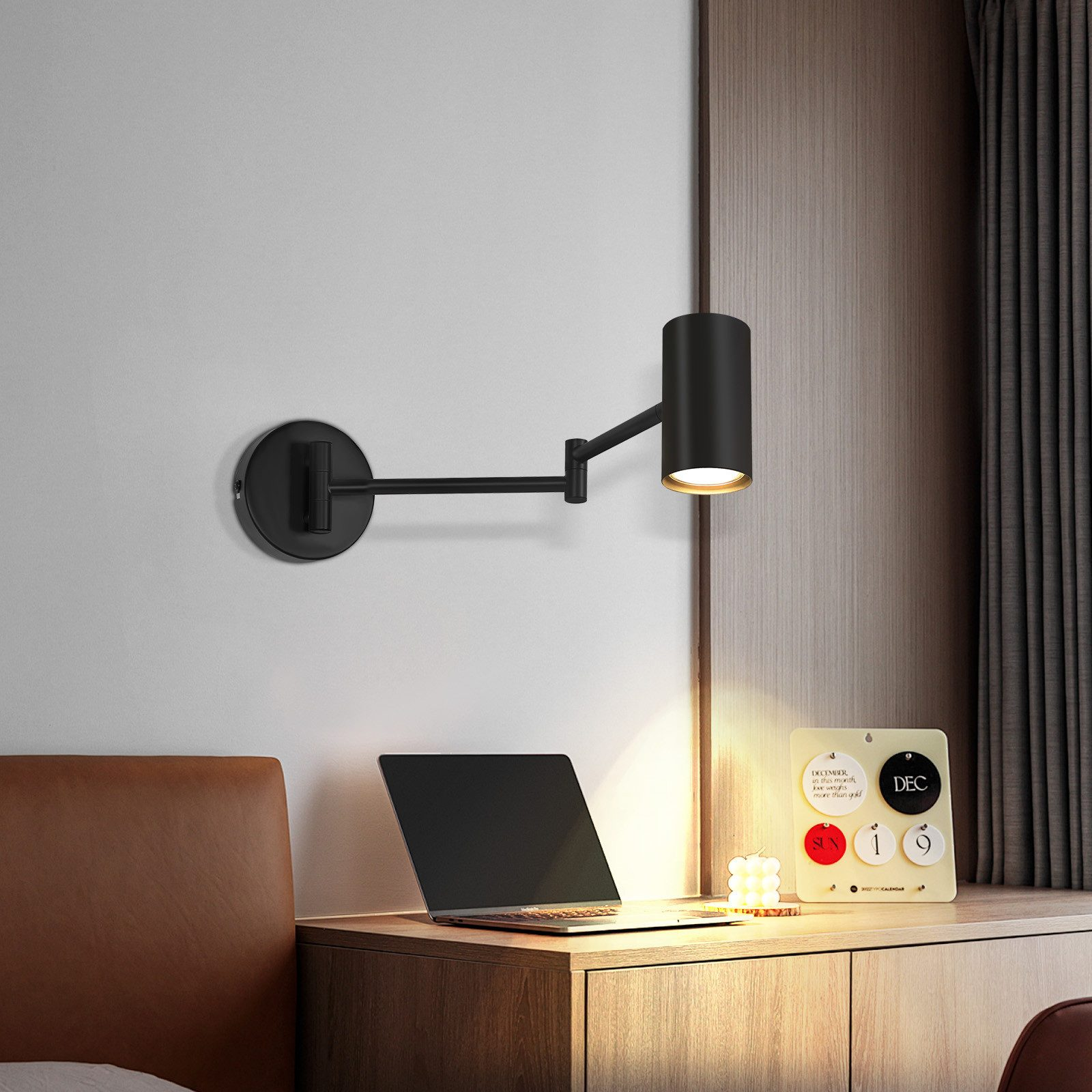 Czarna lampa ścienna z laptopem i kalendarzem biurkowym. W tle znajduje się łóżko.