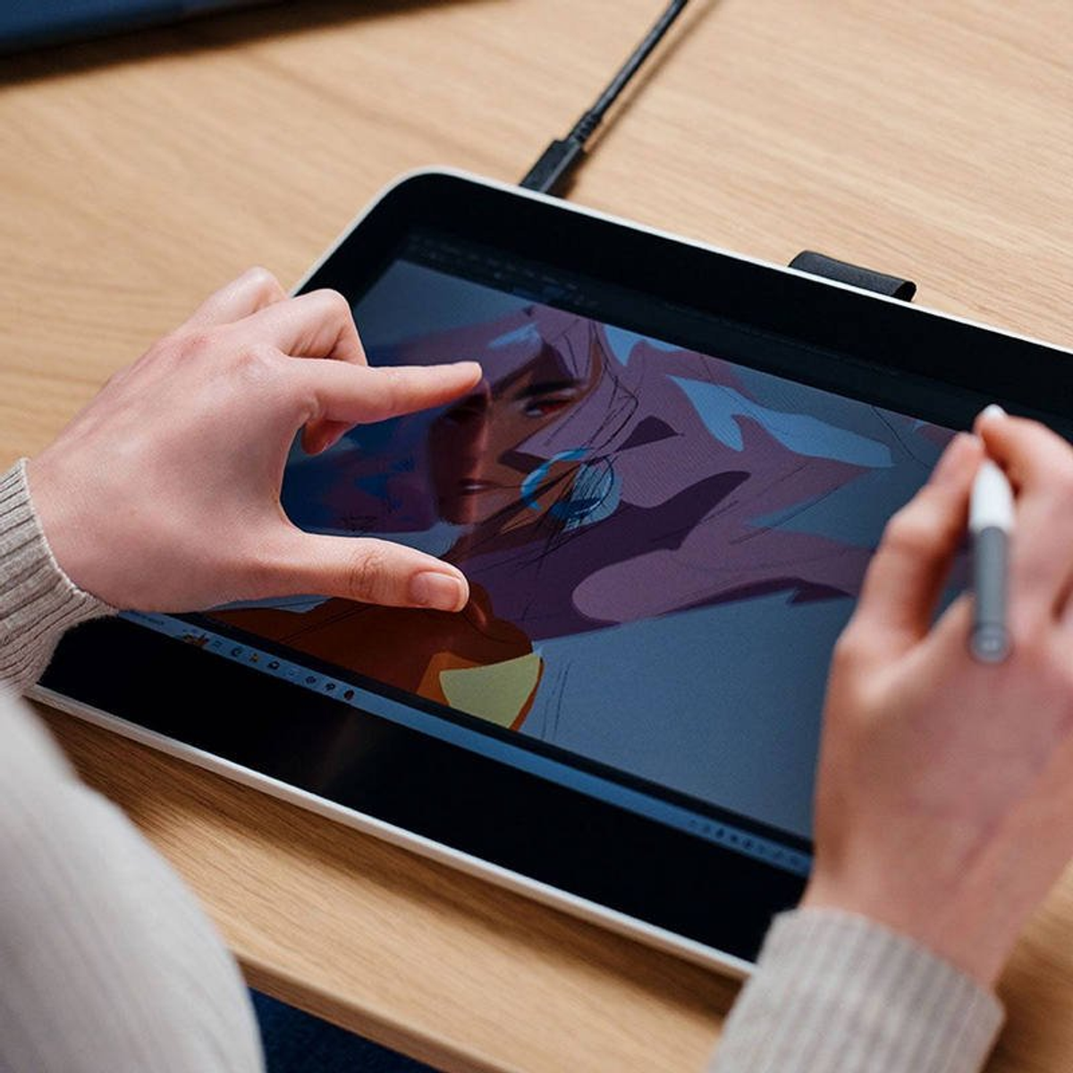 Ręka z rysikiem na tablecie z grafiką cyfrową, na drewnianej powierzchni.
