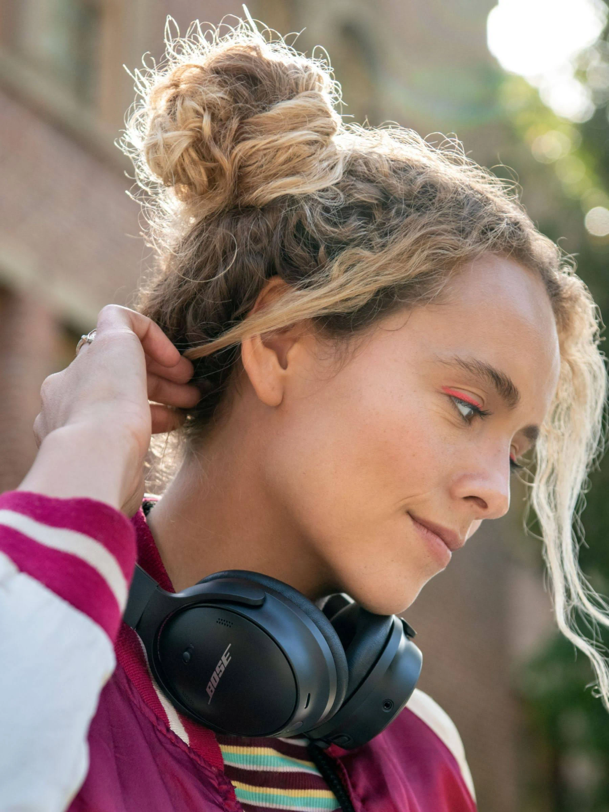 Kobieta trzymająca włosy, nosząca czarne słuchawki Bose. Jasne tło.