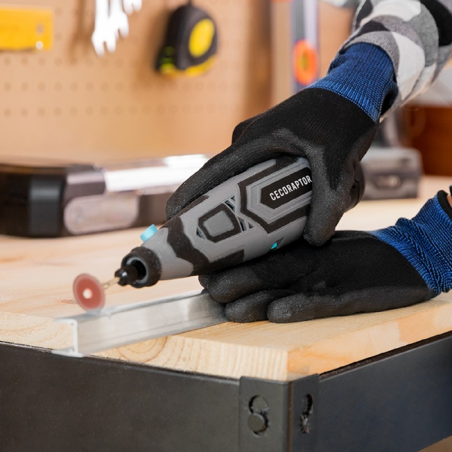 Persona con guantes negros usando una herramienta rotativa en una superficie de madera cerca de herramientas.