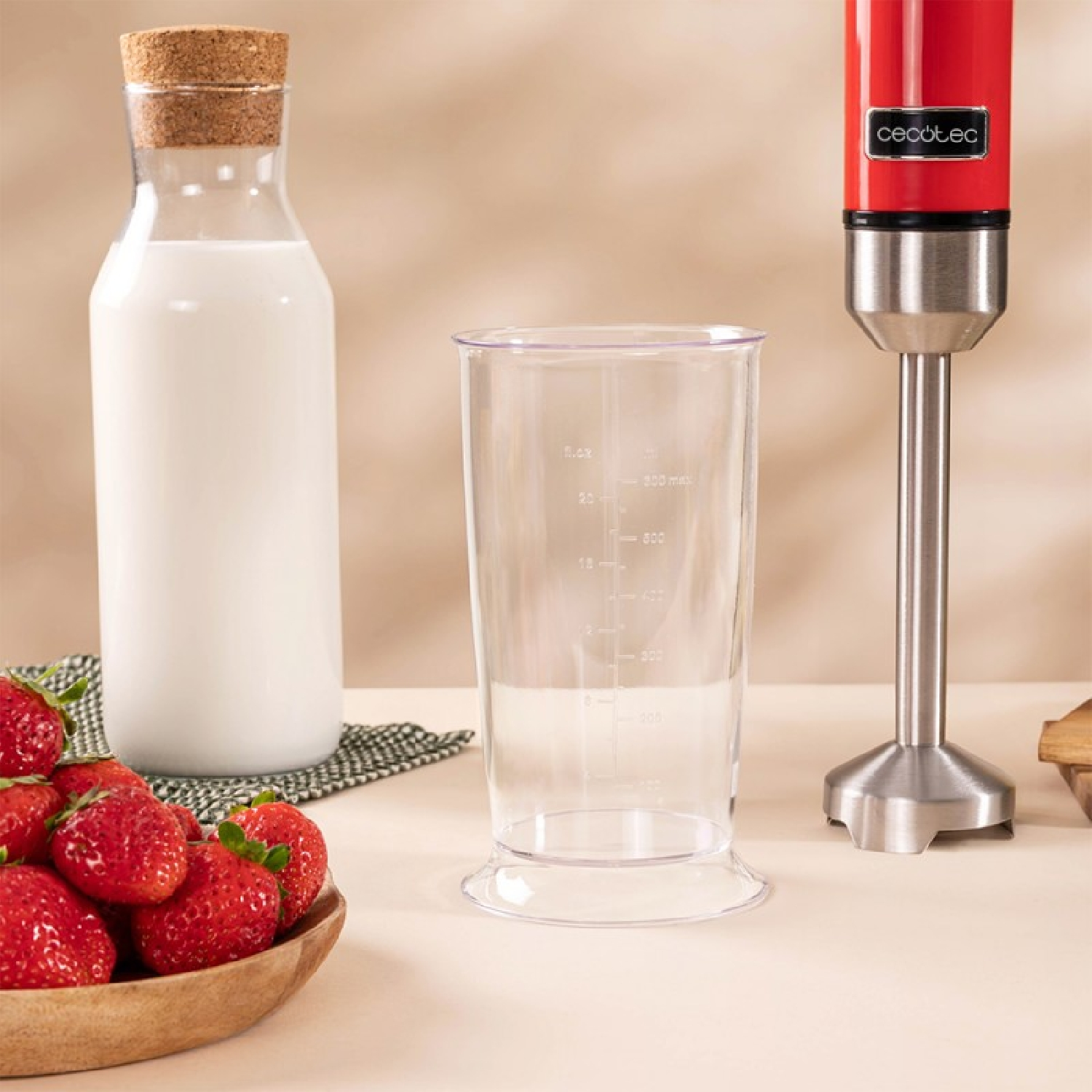 Un frullatore, un bicchiere, una bottiglia di latte e fragole sono su una superficie beige.
