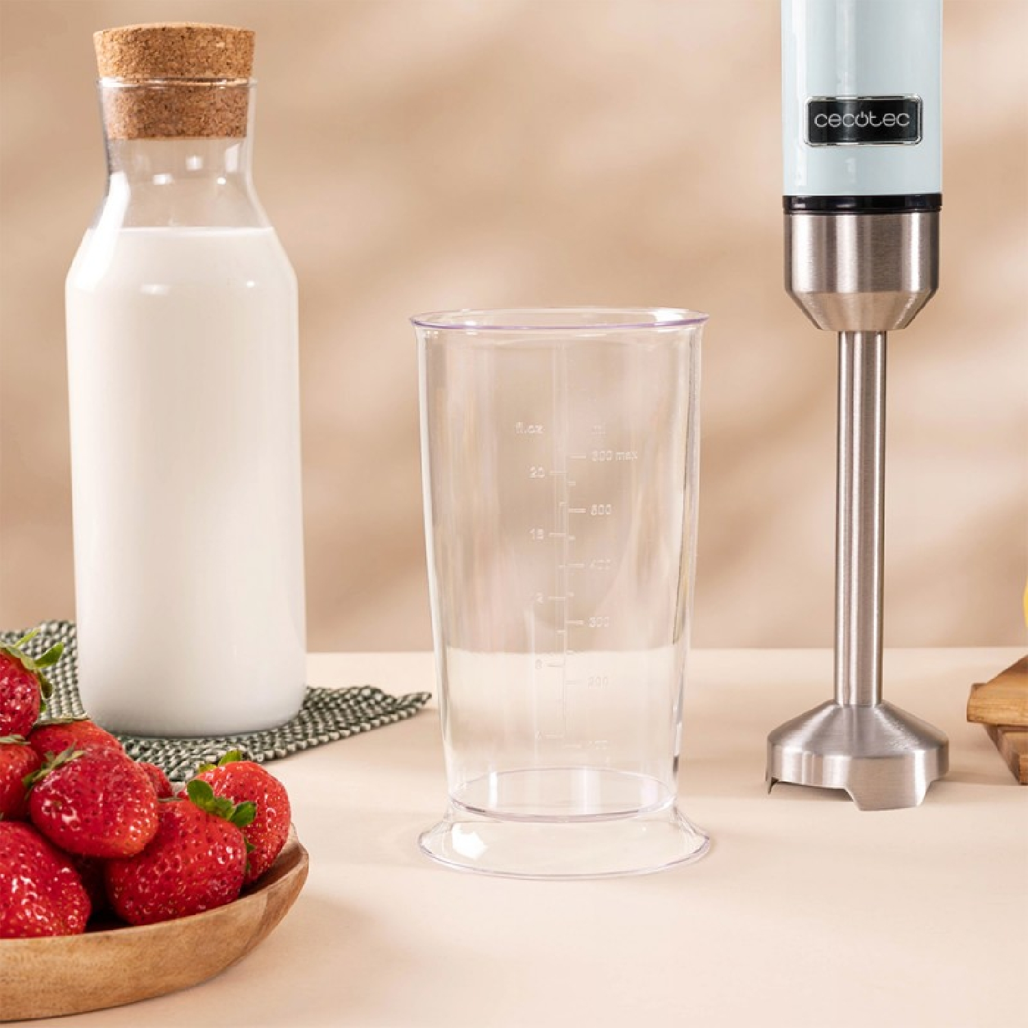 Una bottiglia di latte, un misurino e un frullatore a immersione con fragole.