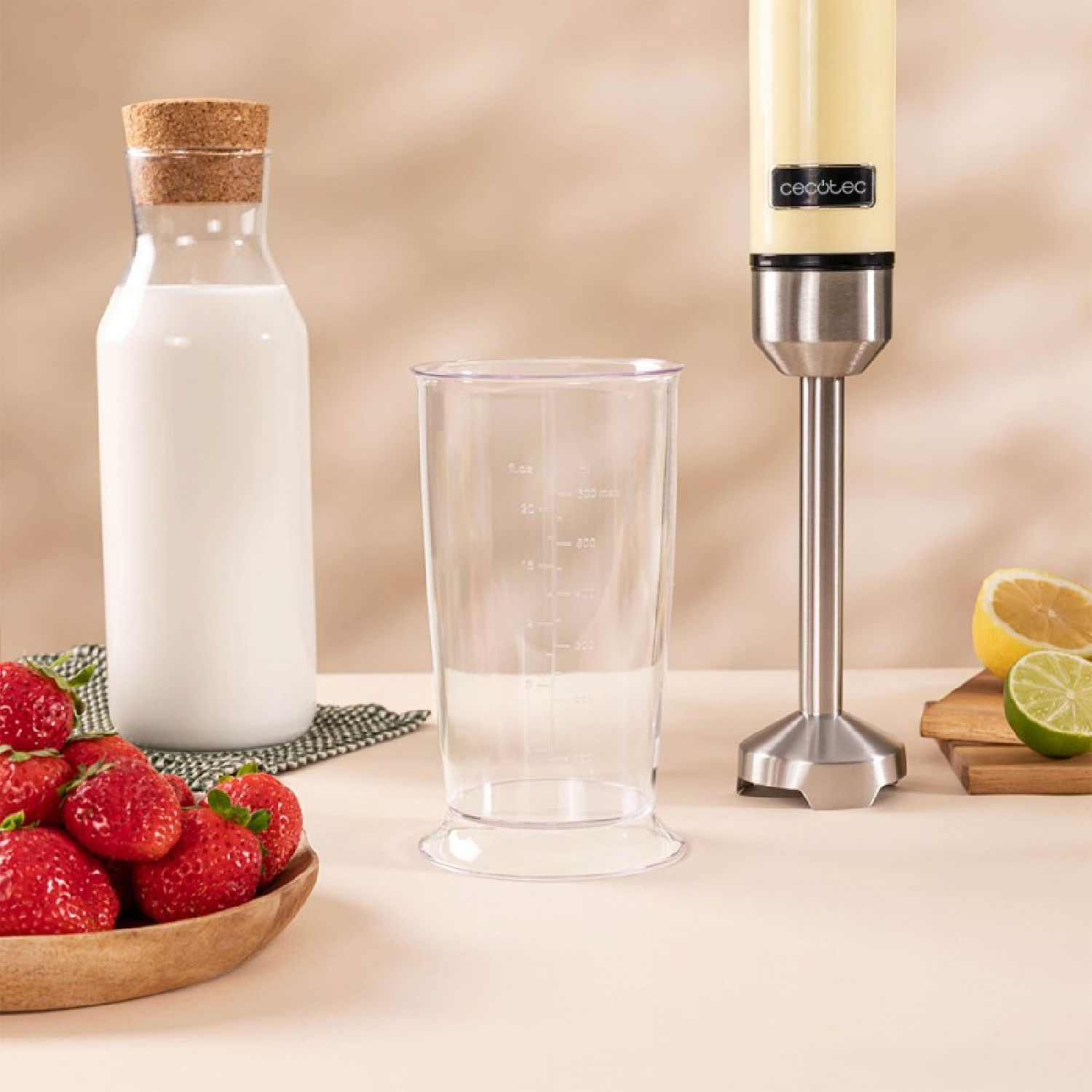 Un frullatore, un bicchiere, una bottiglia di latte, fragole, limone e lime su superficie beige.