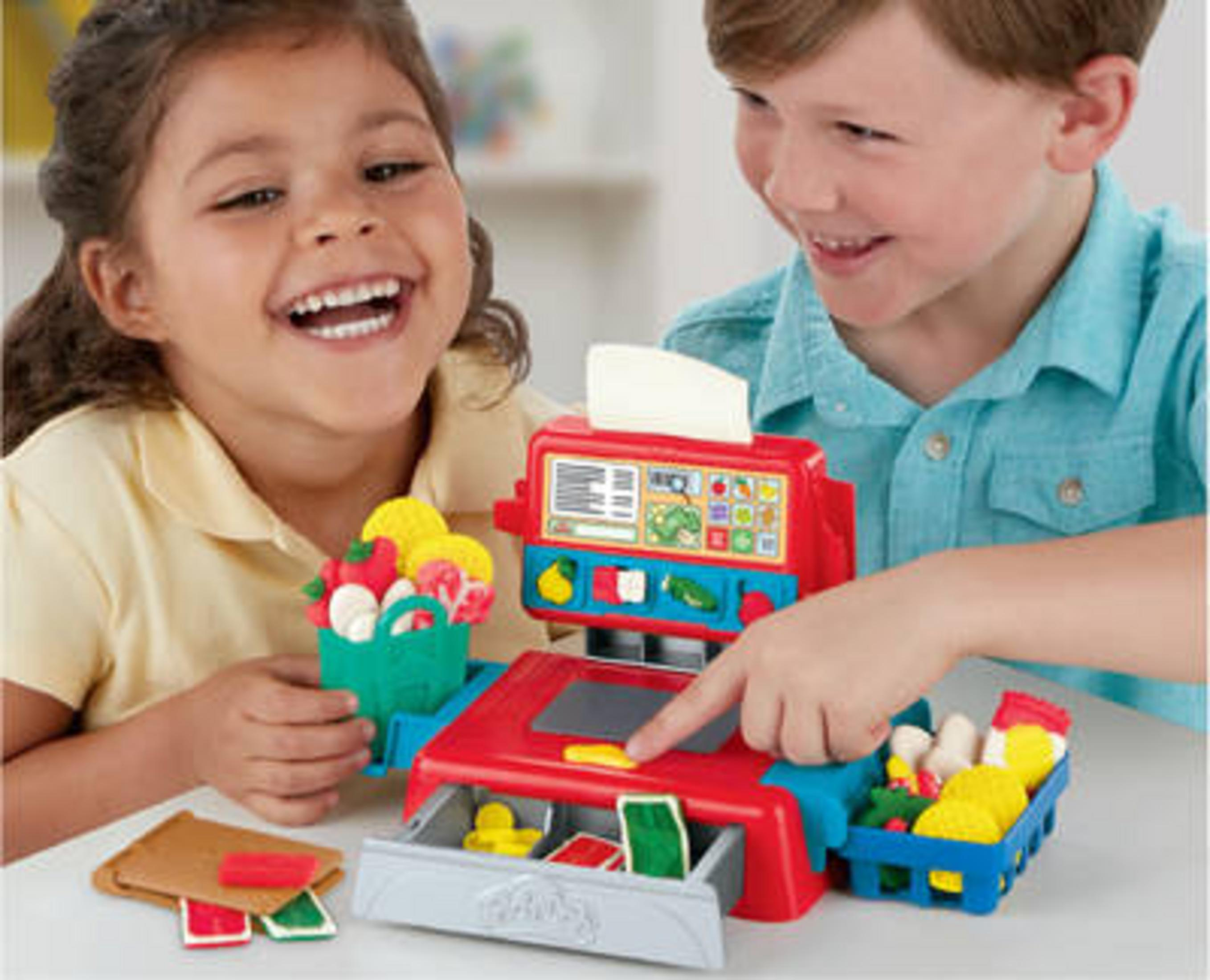 Dos niños jugando con una caja registradora de juguete con alimentos de juguete.