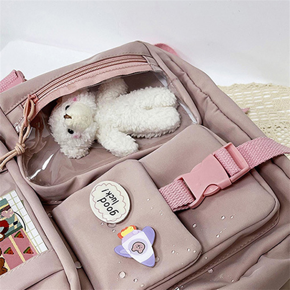 Rosa Rucksack mit Teddybär, Klarsichttasche und mehreren kleinen Taschen mit Abzeichen.