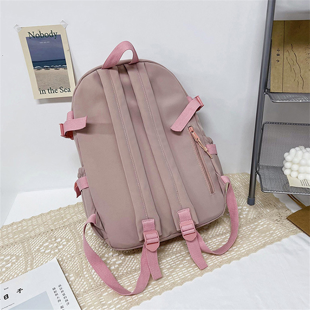 Rucksack mit rosa Trägern. Hat mehrere Taschen. Ein Buch und ein Papier mit Text liegen auf einer weißen Oberfläche.