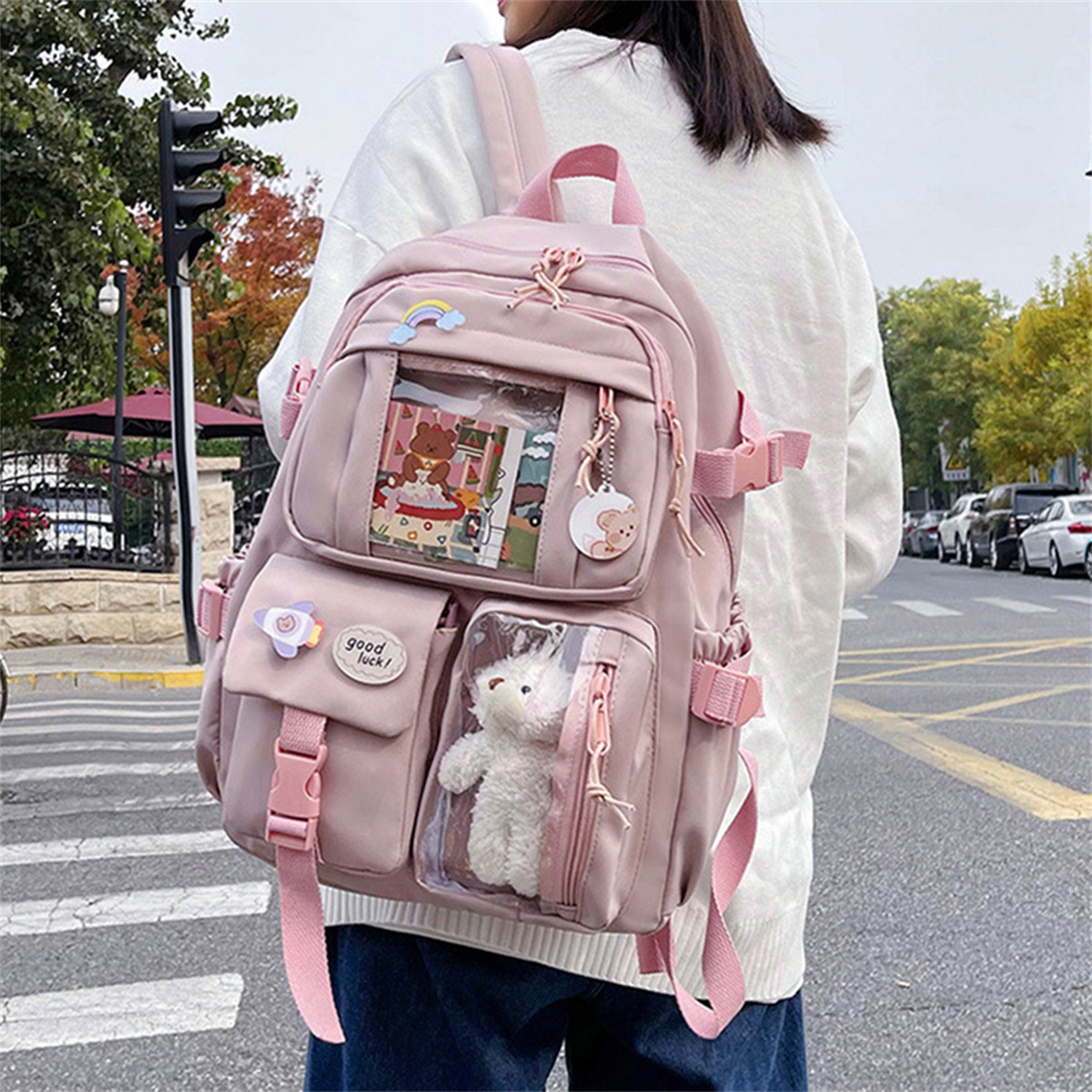 Ein rosa Rucksack mit mehreren Taschen, einem Regenbogen, einem Teddybär und einem Mädchen, das auf der Straße geht.