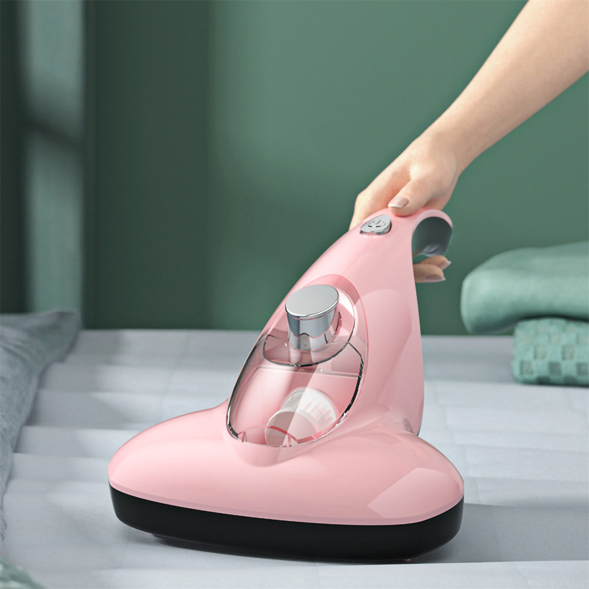 Pinker Handstaubsauger. Menschliche Hand hält den Griff. Weißes Bett im Hintergrund.
