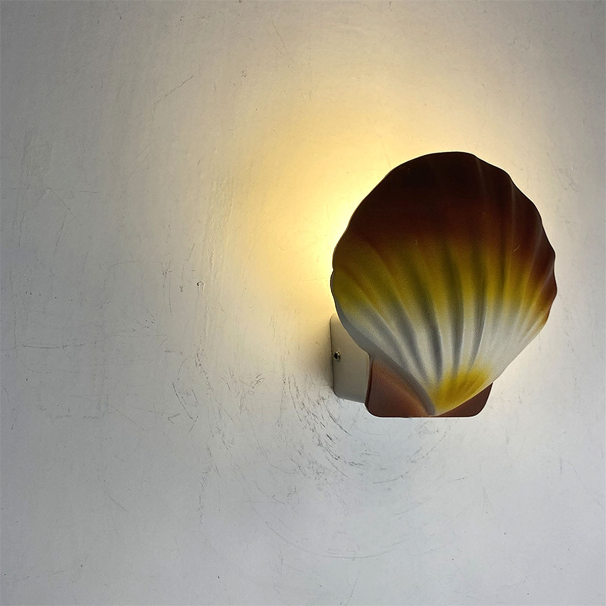 Eine muschelförmige Wandleuchte in warmem, gelblichem Licht, an einer weißen Wand befestigt.