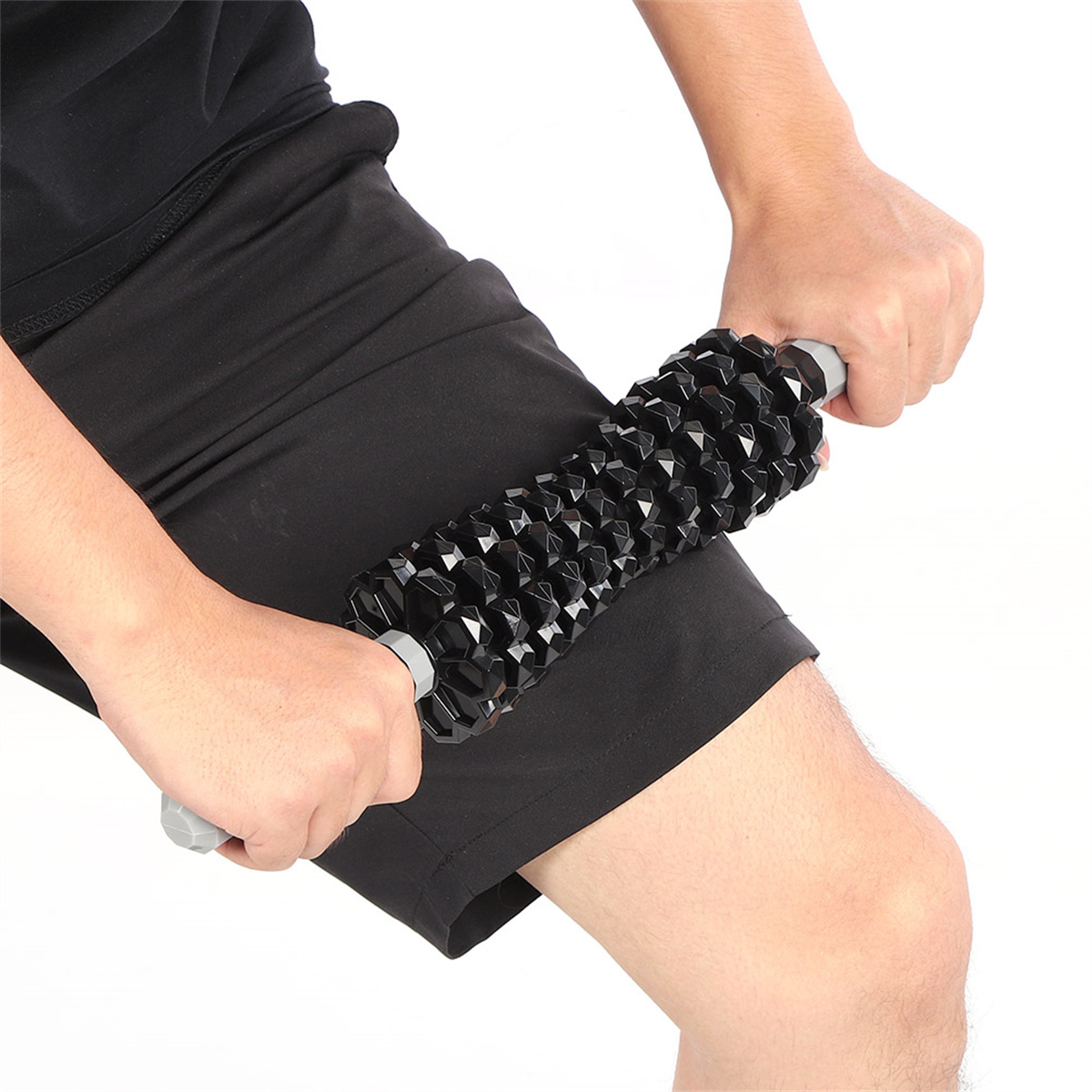 Person benutzt eine Massagerolle an ihrem Oberschenkel. Schwarze Rolle. Person trägt schwarze Shorts.