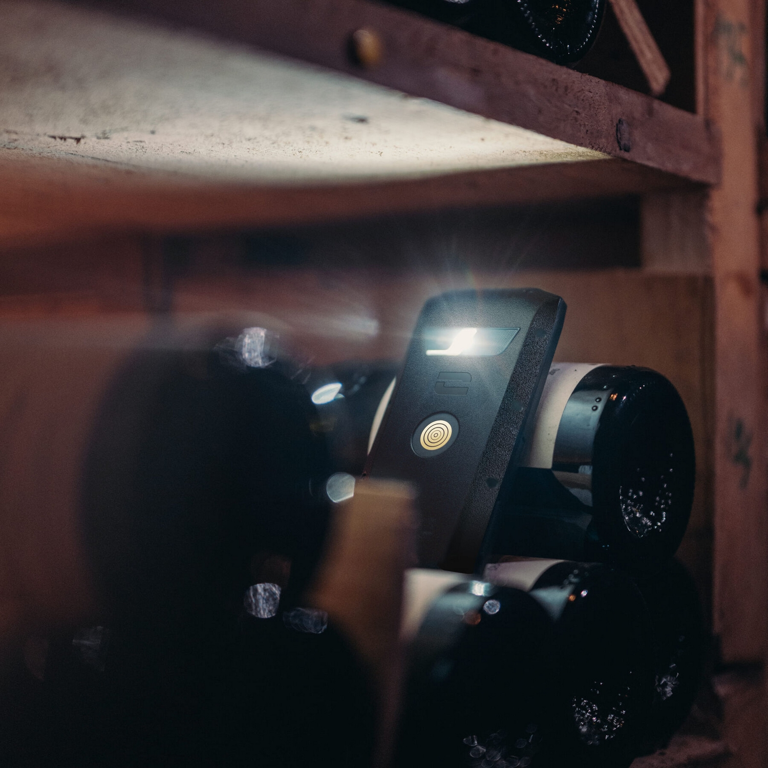 Bottiglie di vino scuro in una cantina. Un dispositivo nero con una luce in primo piano.
