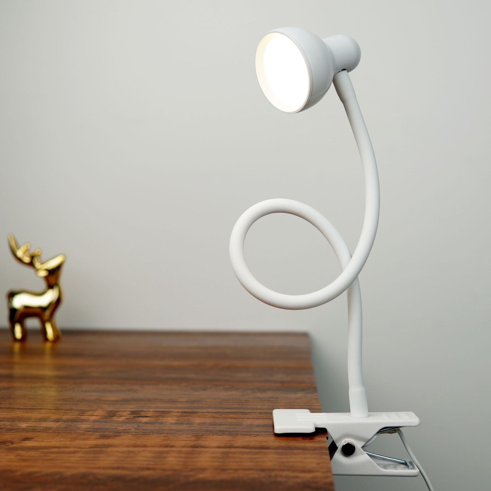 Witte bureaulamp met een flexibele nek, die een houten tafel verlicht.