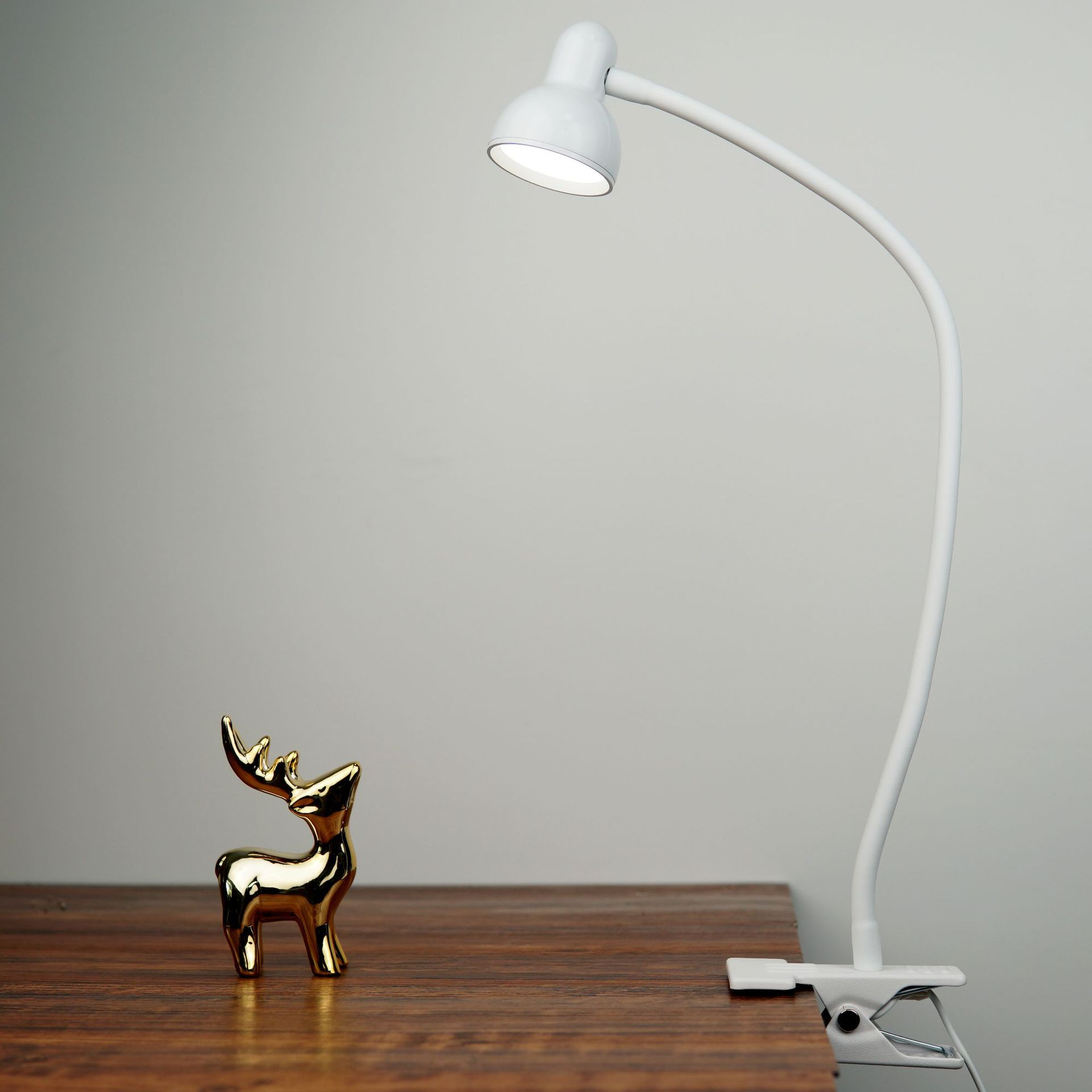 Witte bureaulamp met gouden hertfiguur. De lamp is aan en schijnt.