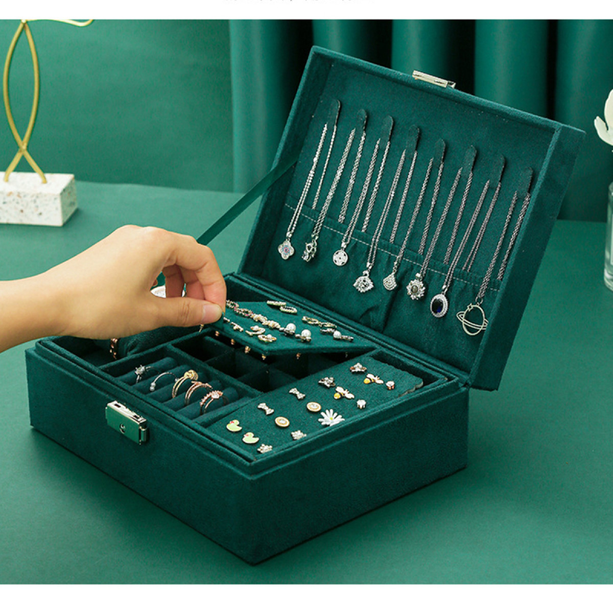 Eine grüne Schmuckschatulle mit Schmuck, und eine Hand, die den Deckel öffnet.