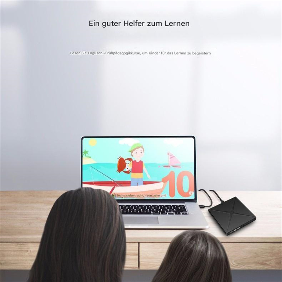 Ein Laptop mit einem farbenfrohen Lernspiel wird von zwei Kindern betrachtet. Eine schwarze Box ist an den Laptop angeschlossen.