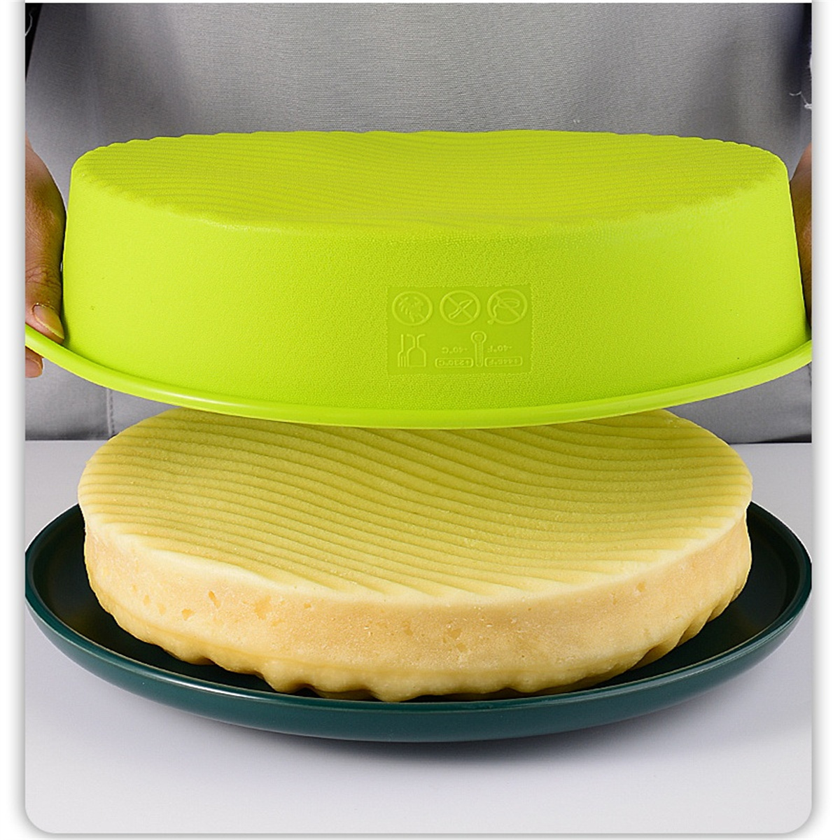 Grüner Deckel über einem runden Kuchen auf dunklem Teller. Hintergrund: weiß.