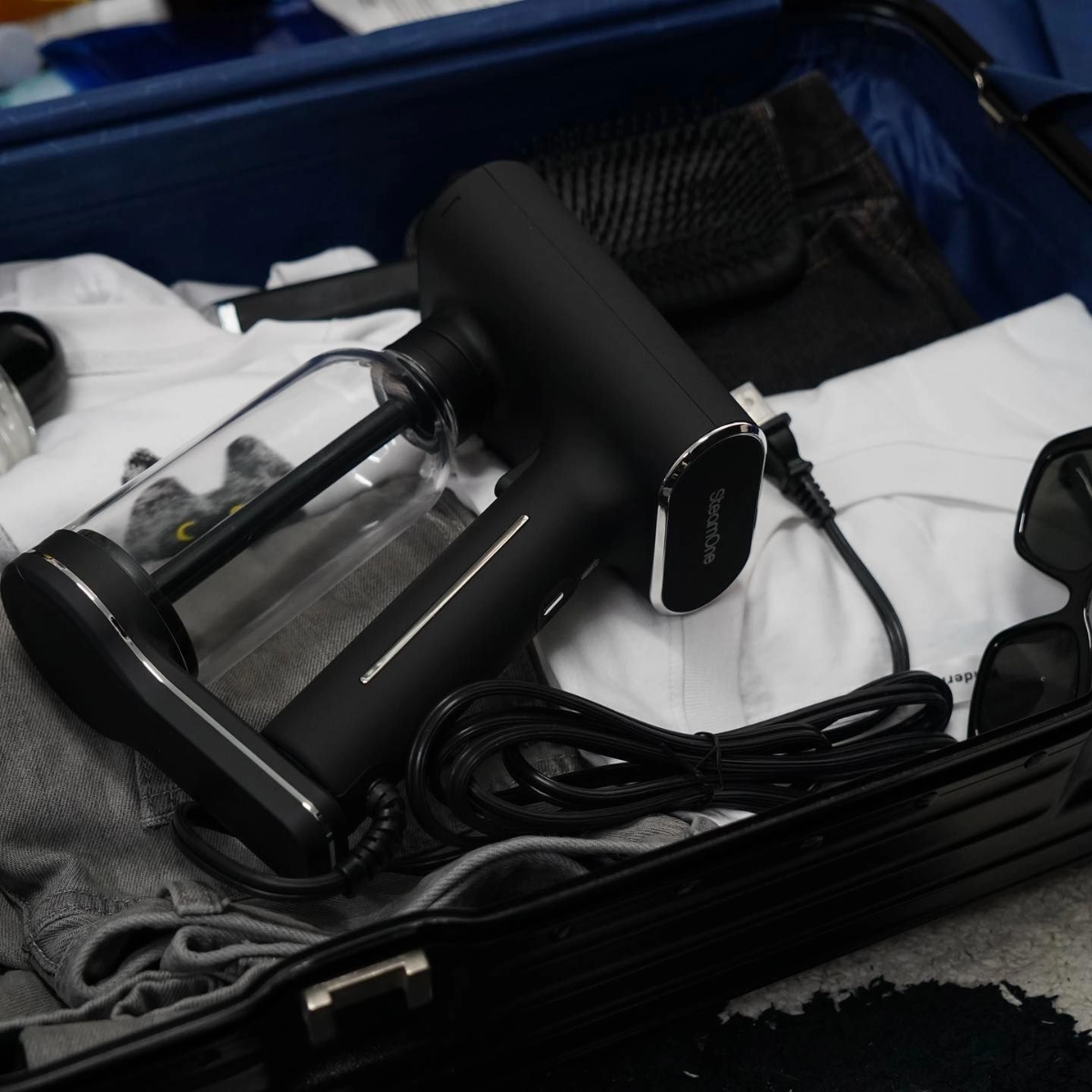 Un défroisseur à main noir dans une valise avec des vêtements et d'autres articles.