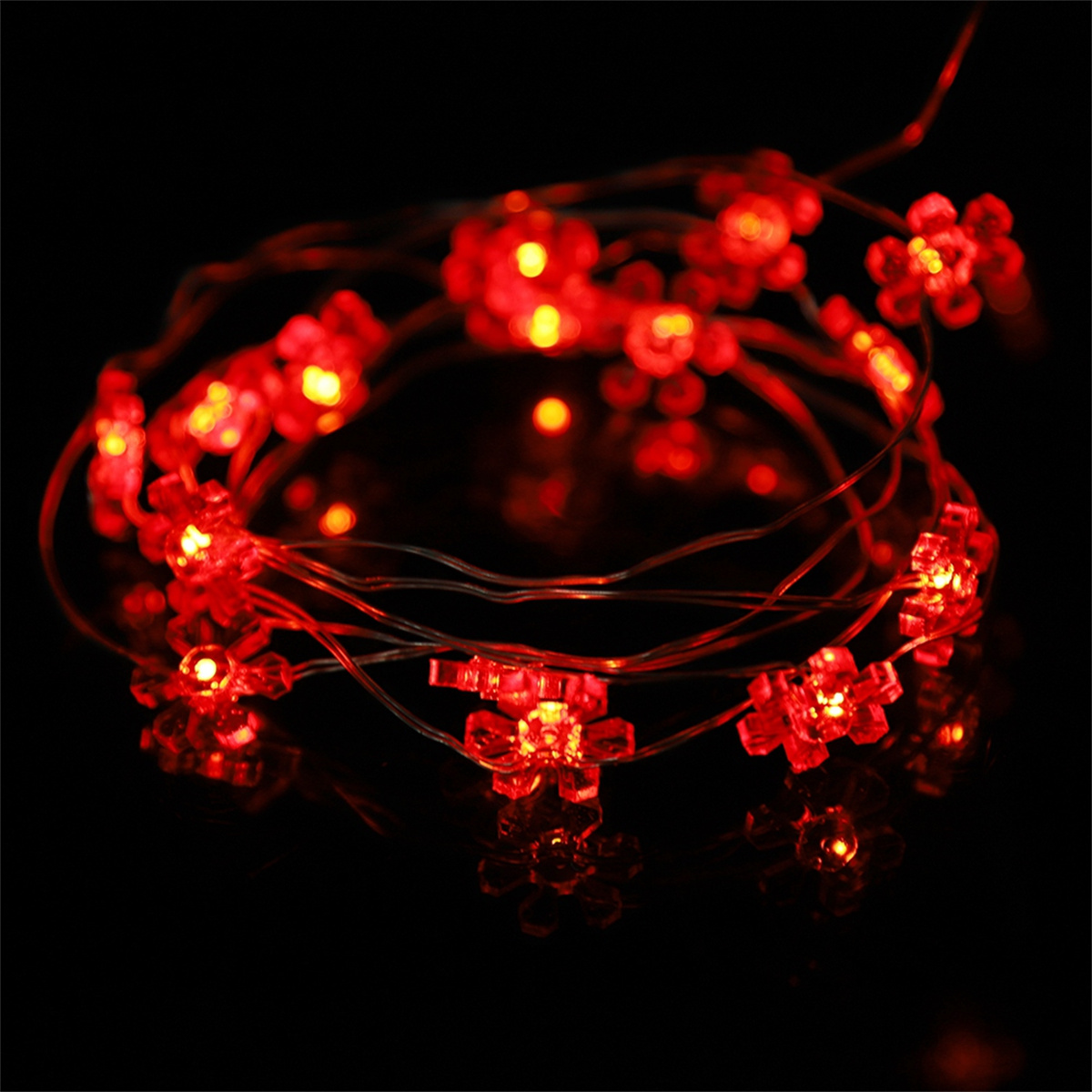 Eine Lichterkette mit roten, blütenförmigen LEDs auf schwarzem, reflektierendem Untergrund.