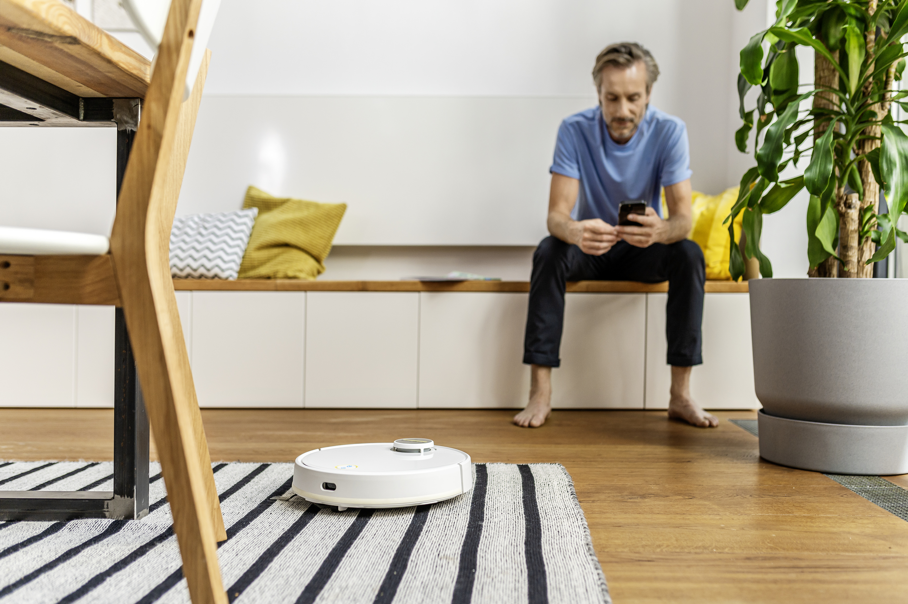 Widok z góry na biały robot sprzątający o okrągłym kształcie, na drewnianej podłodze.