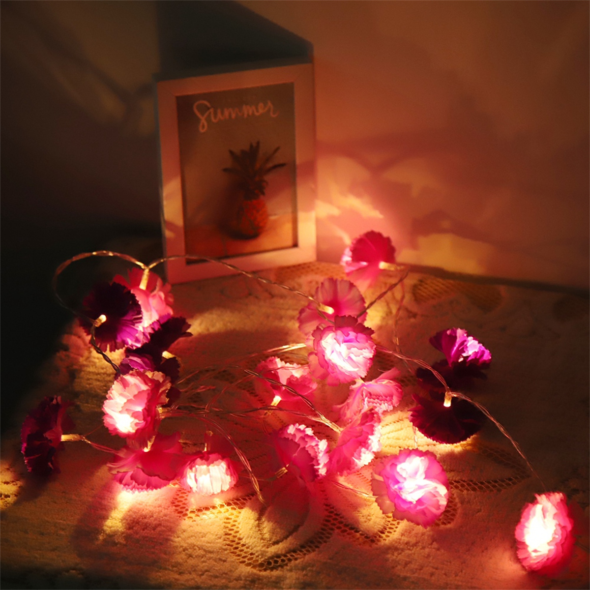 Lichterkette mit rosa Blüten und einem Bilderrahmen mit einer Ananas-Illustration.
