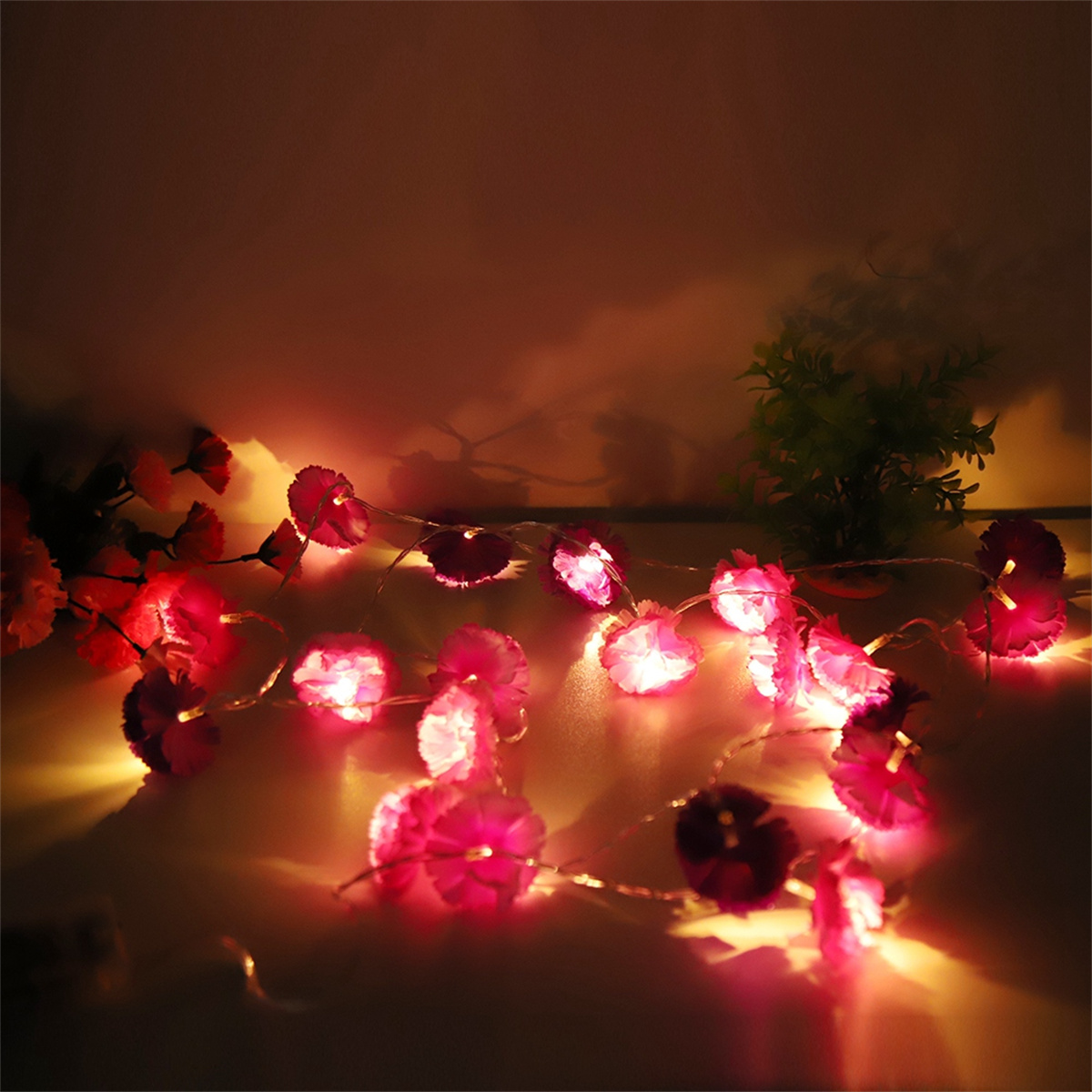 Nahaufnahme einer Lichterkette mit rosa blütenförmigen Lichtern auf braunem Untergrund.