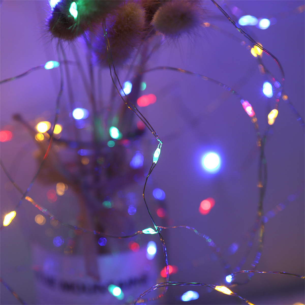Nahaufnahme von Lichterketten mit einer Vase getrockneter Blumen im Hintergrund. Die Lichter sind blau und grün.