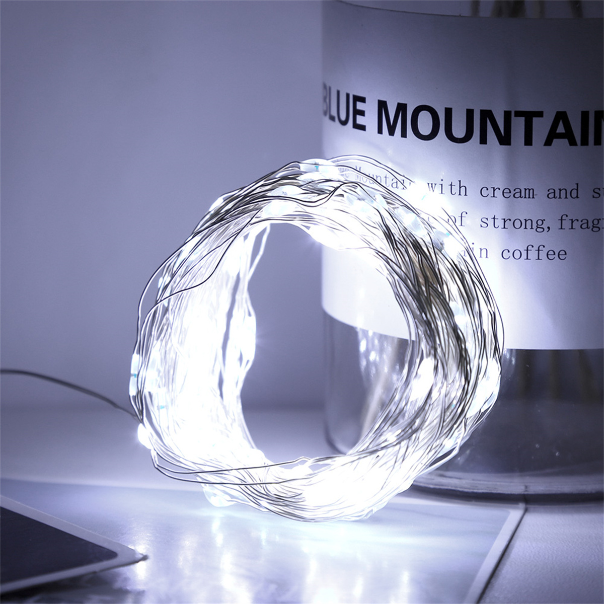 Weiße Lichterkette in einer Spule gewickelt. Eine Flasche mit Schriftzug ist im Hintergrund.