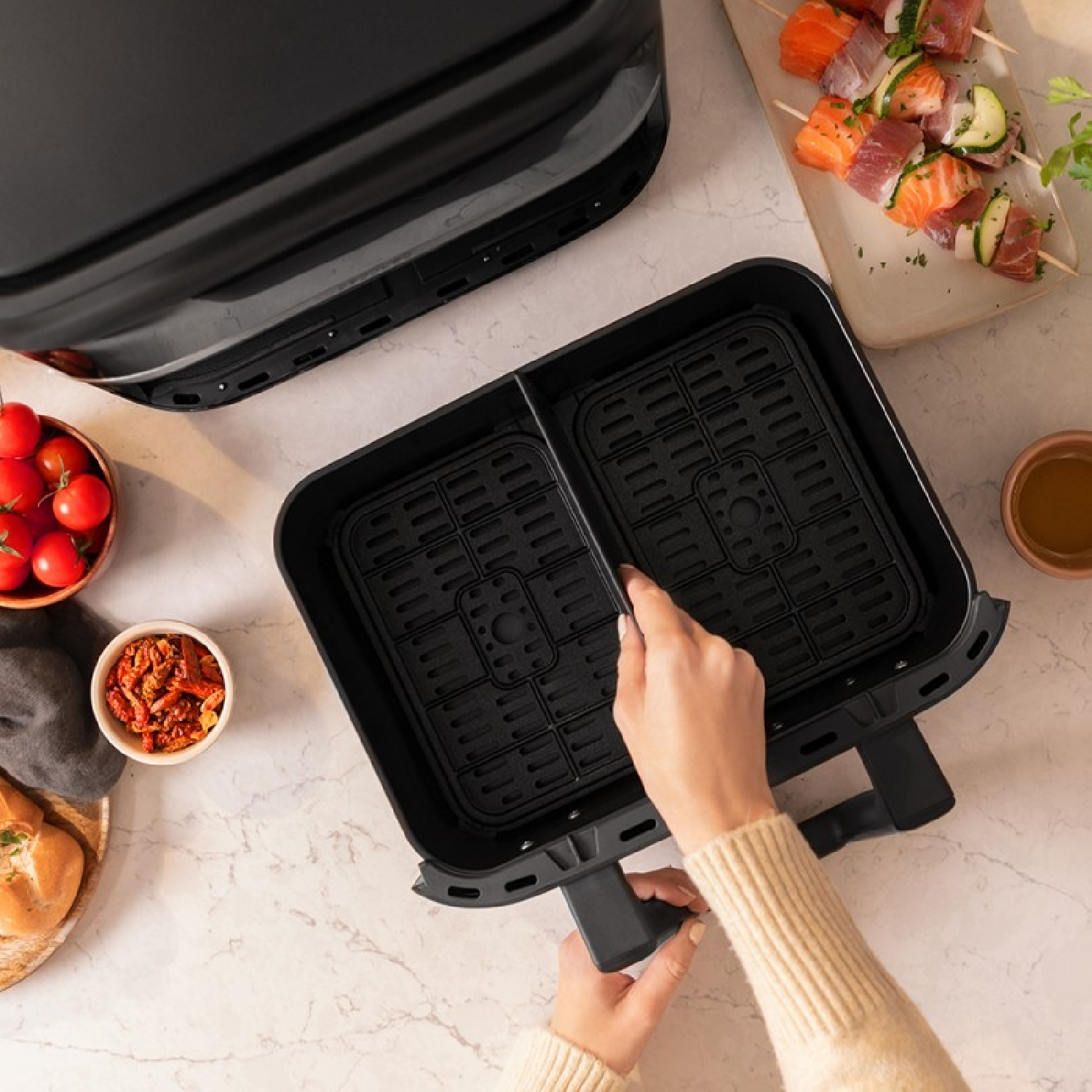 Airfryer met eten erin en handen die hem gebruiken. Daarnaast tomaten, zalm en brood.