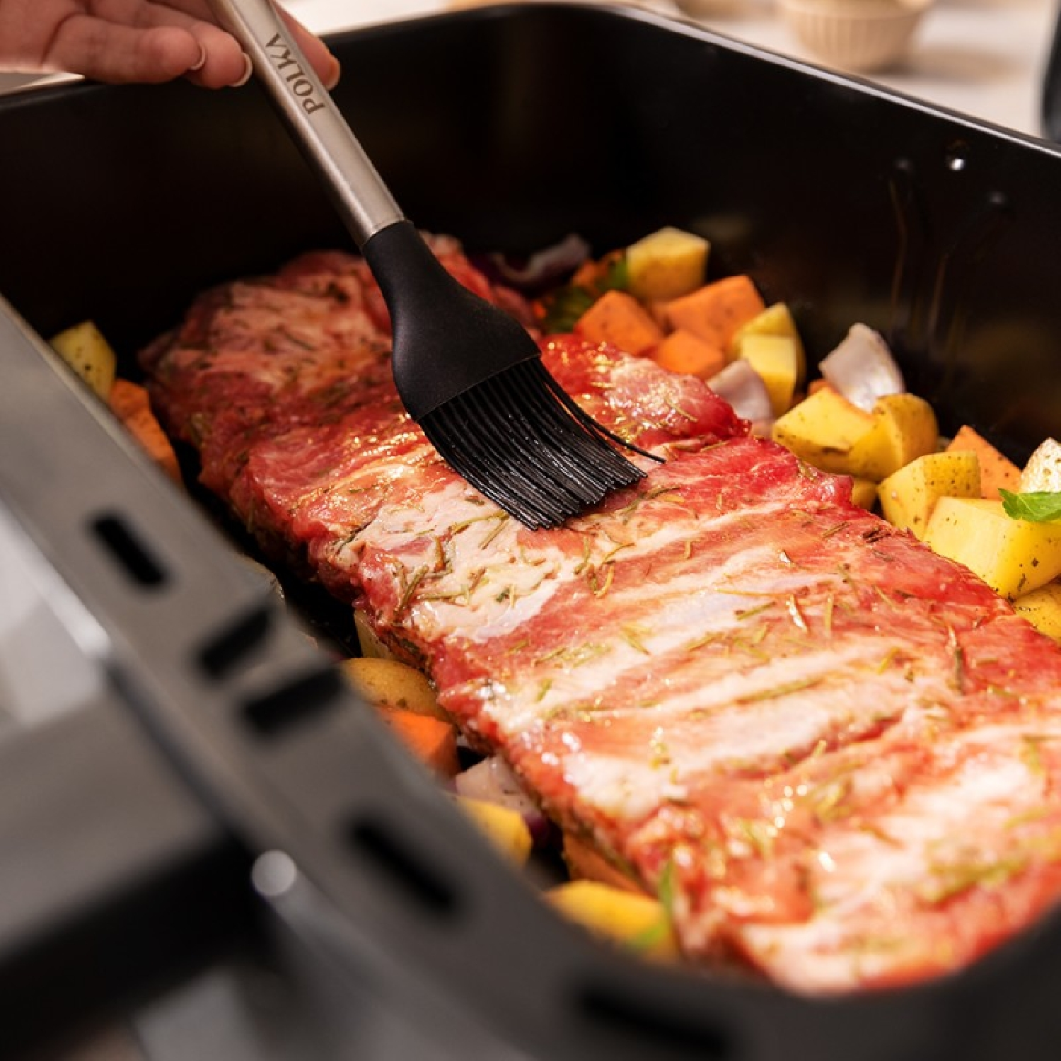 Ribben in een pan die met een kwast worden bestreken, omringd door groenten.