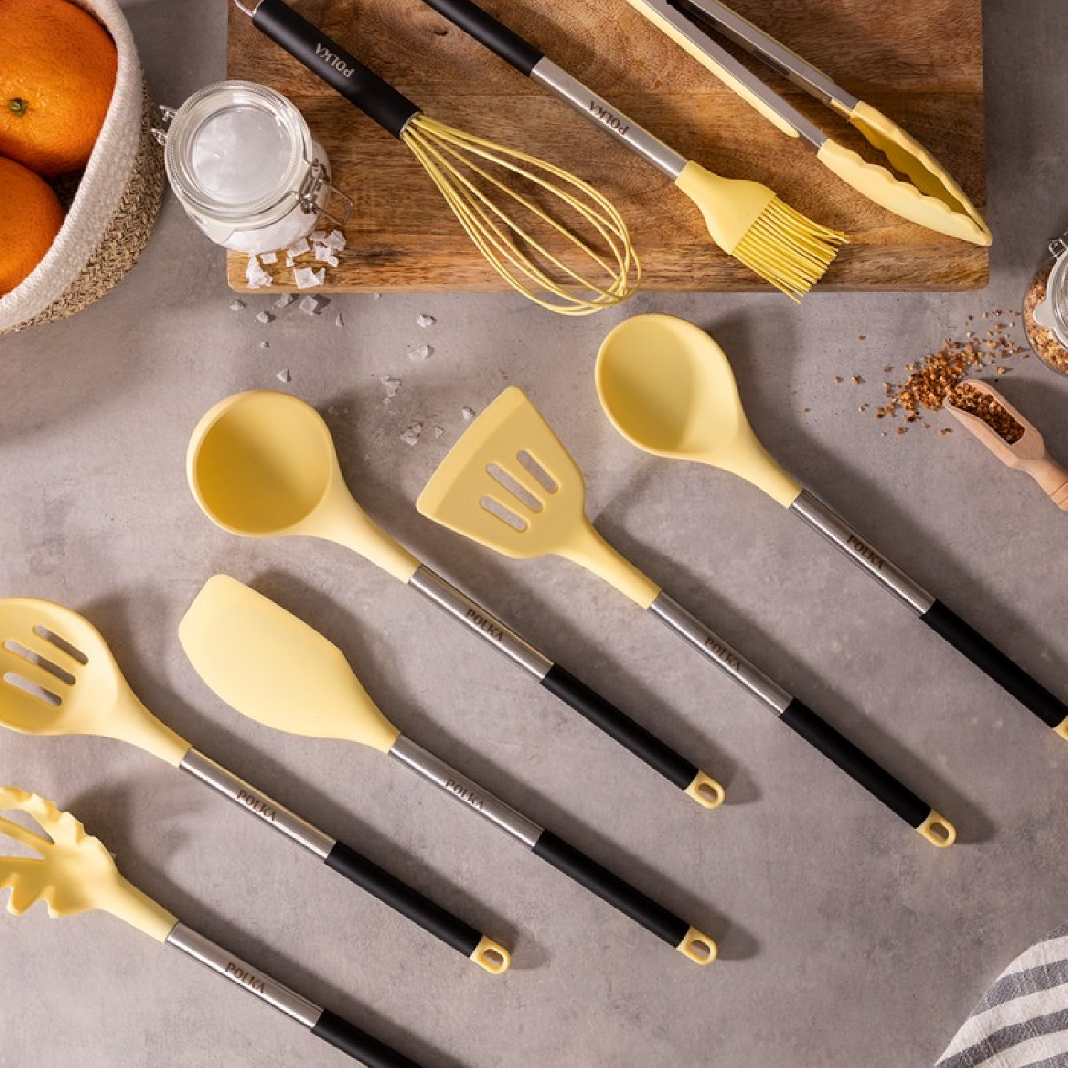 Juego de utensilios de cocina sobre una superficie gris. Incluye espátula, cuchara, pinzas, batidor y más.