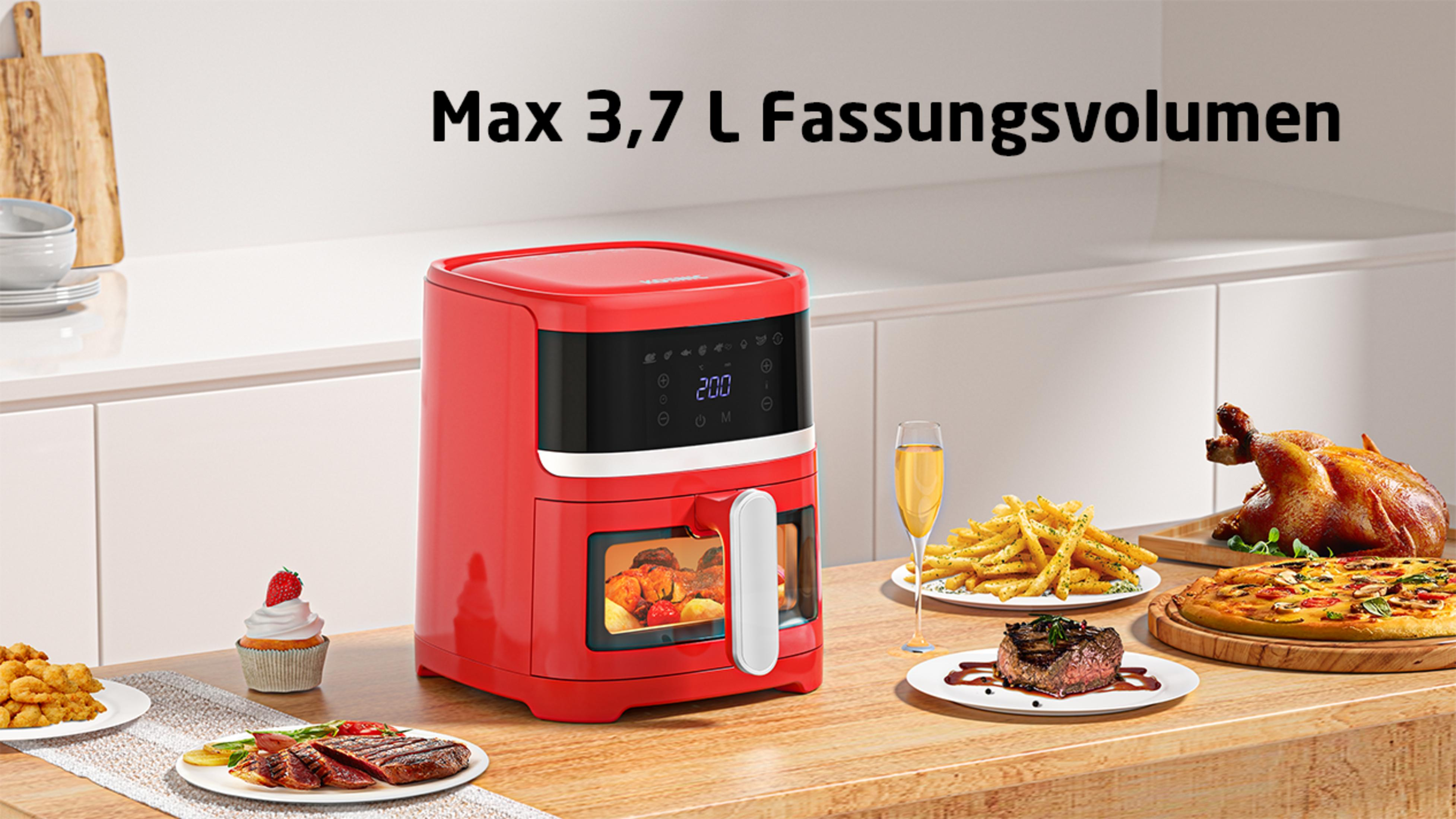 Roter Luftfritteuse mit Essen auf einem Holztisch. Enthält Pommes, Steak und einen Kuchen.