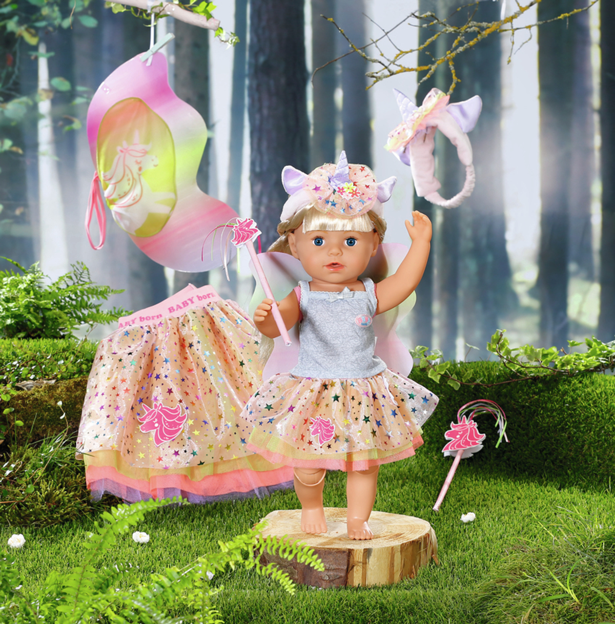 Puppe im Feen-Outfit steht auf Holzscheibe. Zubehör: Flügel, Zauberstab und Rock, in einer Waldkulisse.