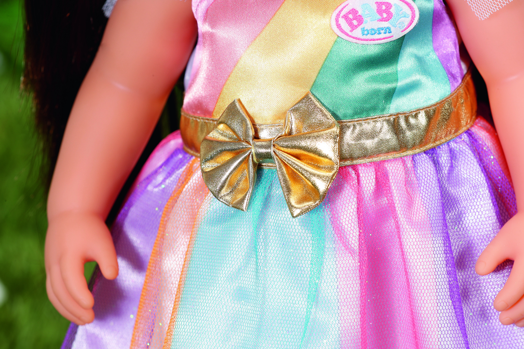Eine Puppe in einem bunten Kleid mit einer goldenen Schleife und einem goldenen Schärpe. Die Haut der Puppe ist hell.