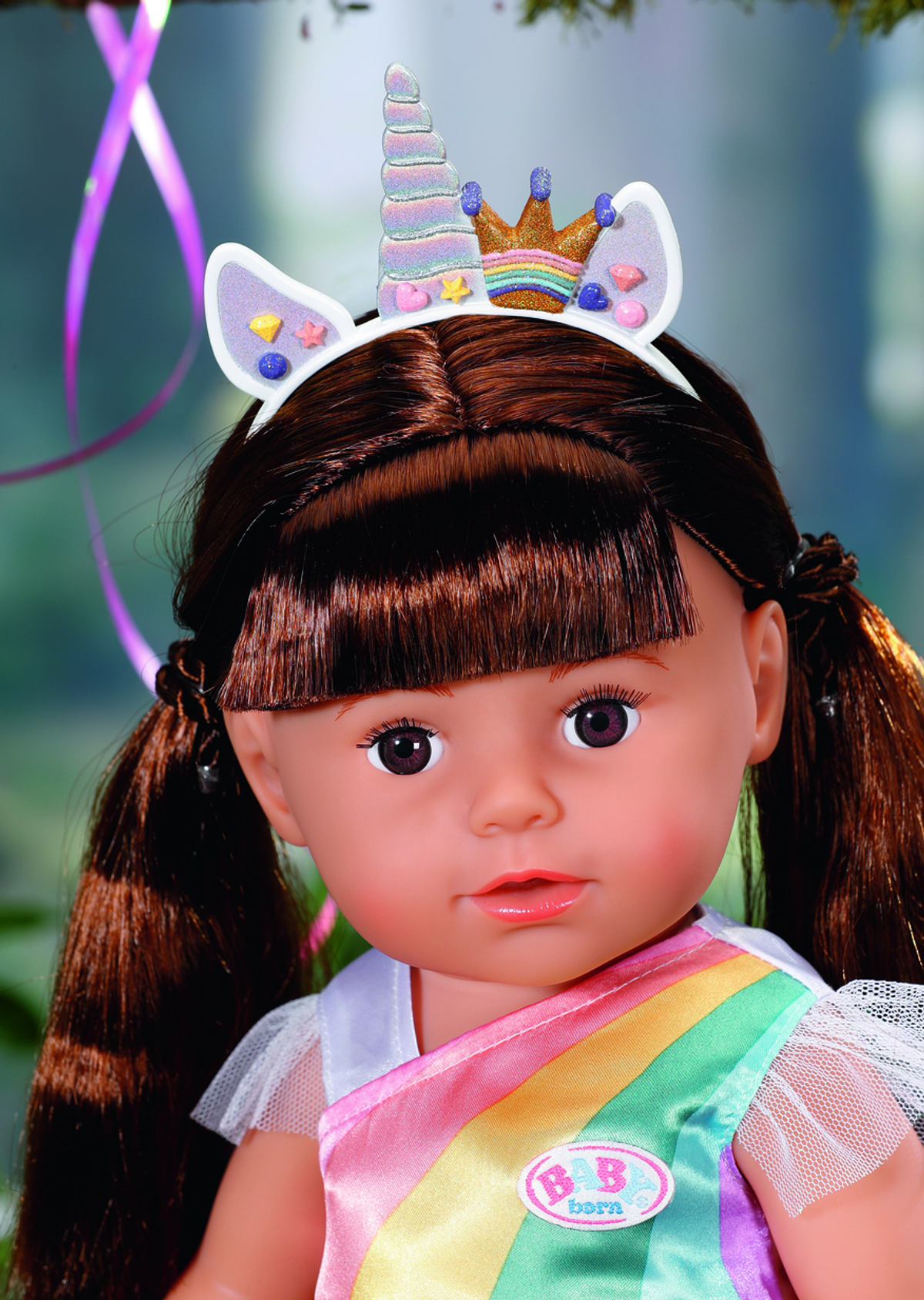 Puppe mit braunen Haaren und Einhorn-Stirnband, Regenbogenkleid. Hintergrund grün.