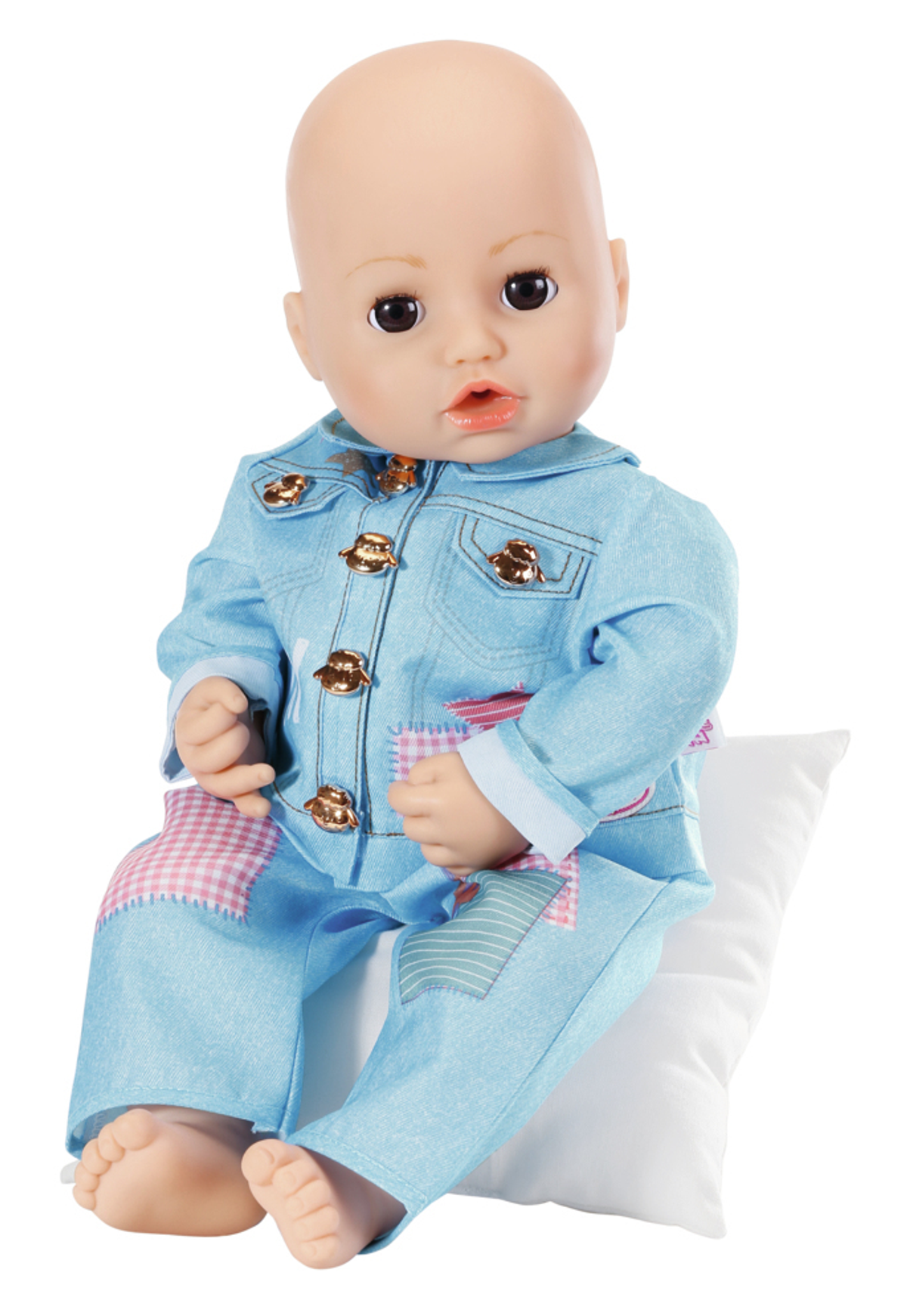 Puppe in jeansartigem Outfit, sitzt auf weißem Kissen vor weißem Hintergrund.